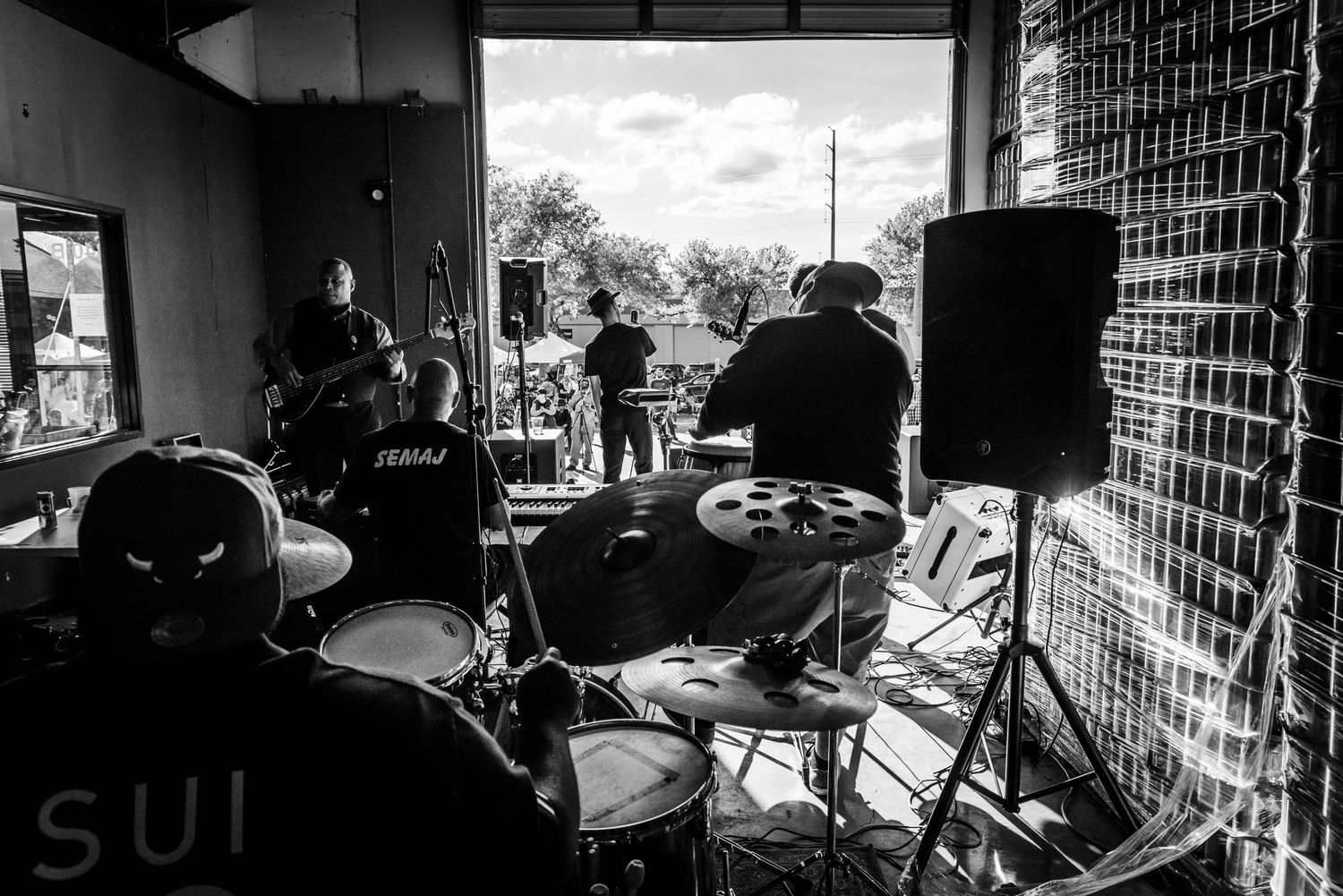 Black and white photo of drum kit setup with speakers and equipment on stage.
