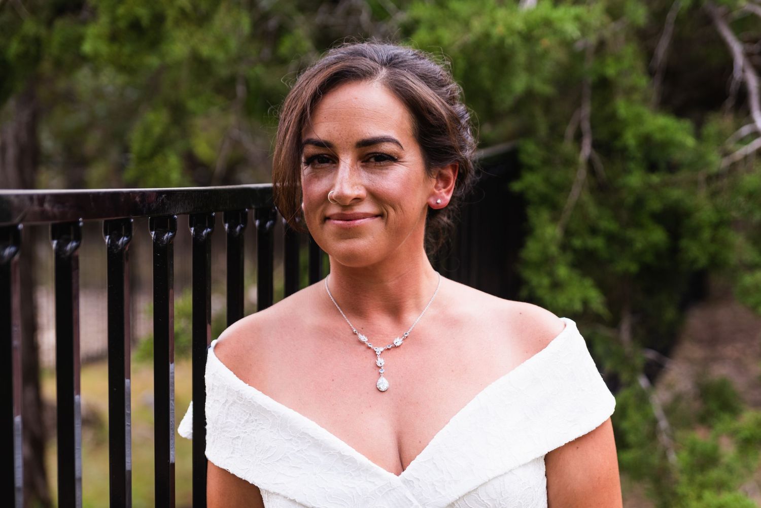 Beautiful off-shoulder wedding dress with delicate necklace in outdoor setting.