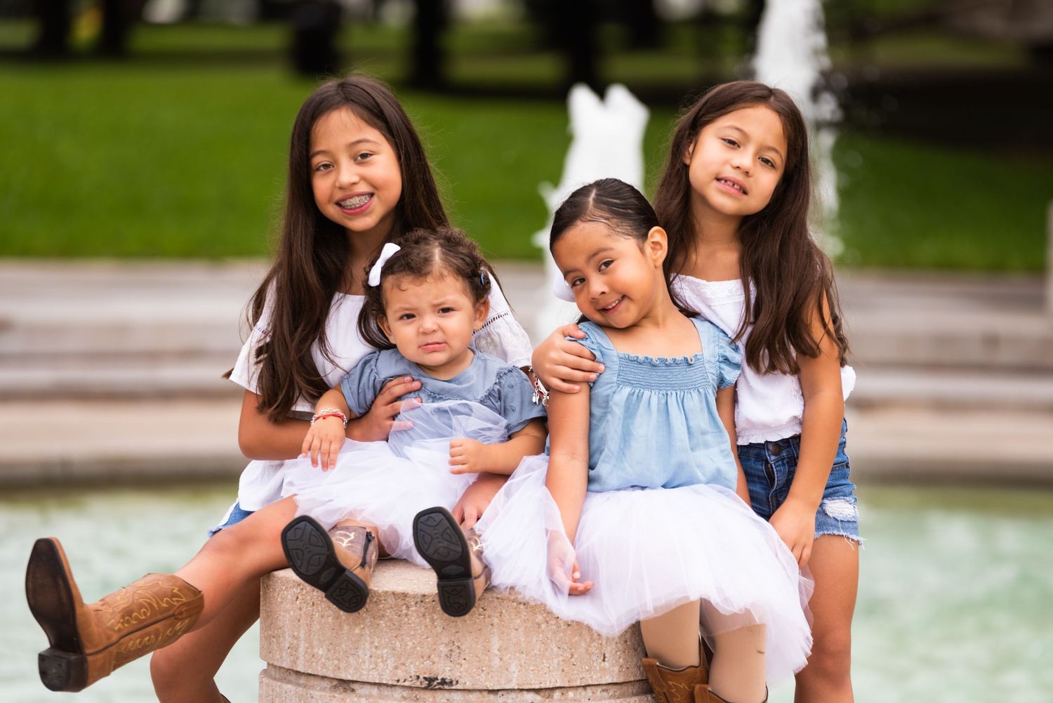 Children sitting together and smiling by fountain on sunny day at park.
