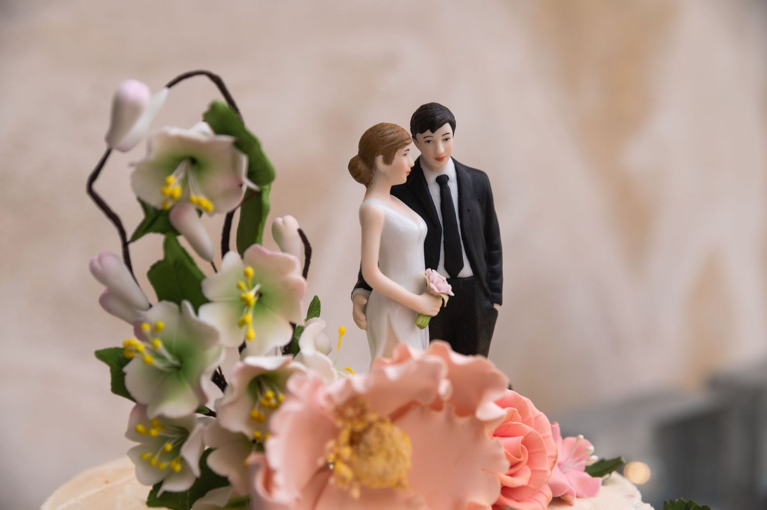 Wedding cake topper figurines nestled among delicate pink and white flowers.