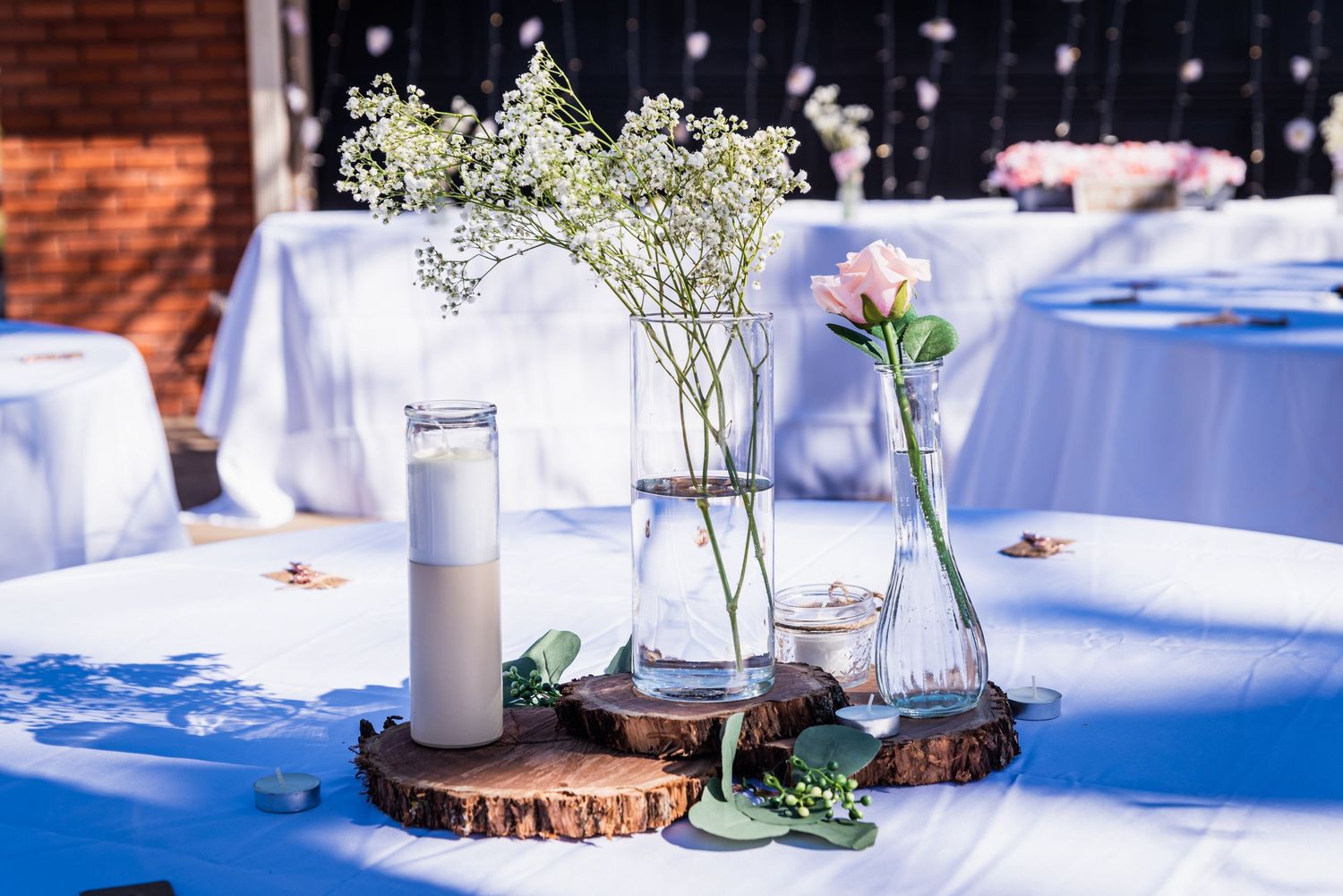 Wedding centerpiece with baby's breath flowers in glass vases on wooden slices with blue tablecloth.
