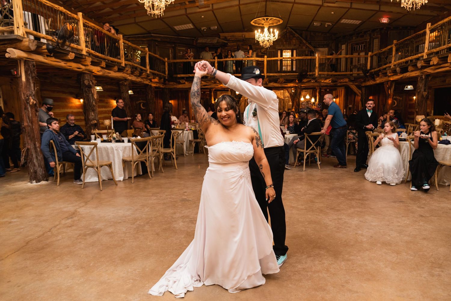 A couple dances in an elegant rustic venue with wooden beams and chandeliers.