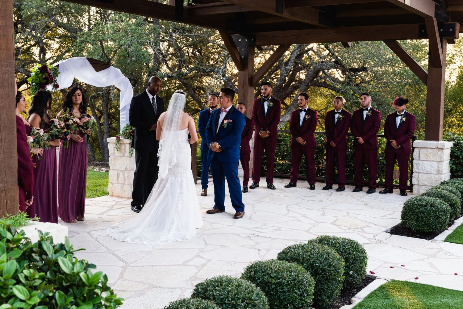 A wedding ceremony under a covered pavilion with burgundy-dressed wedding party members.
