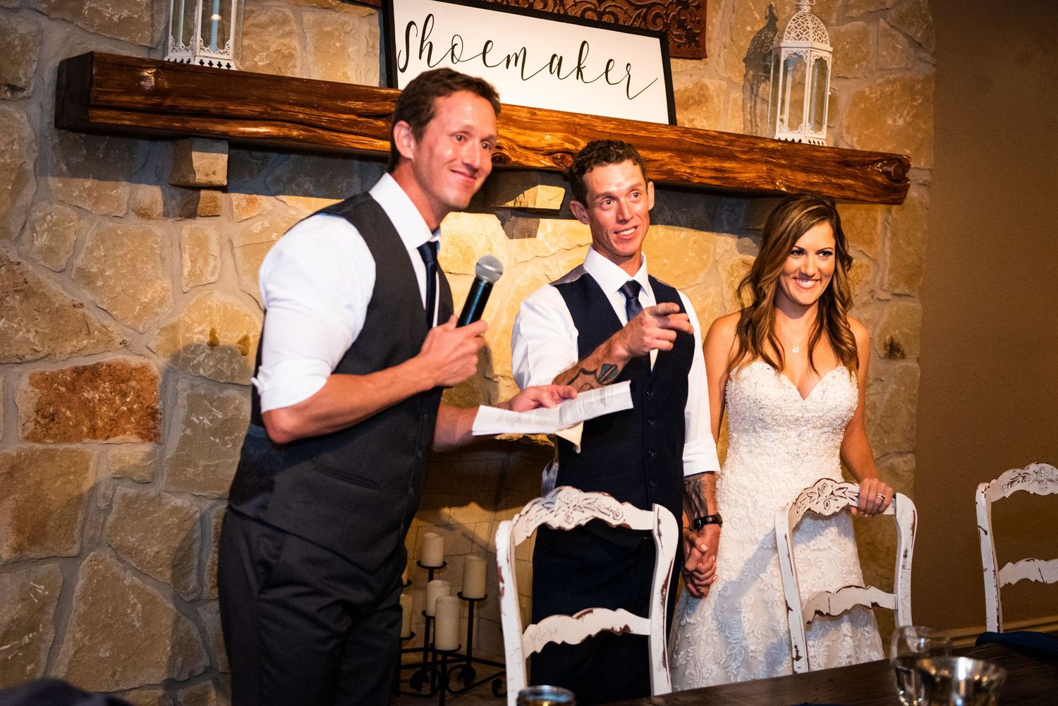 Wedding speeches being delivered in front of a rustic stone wall with wooden beam decor.