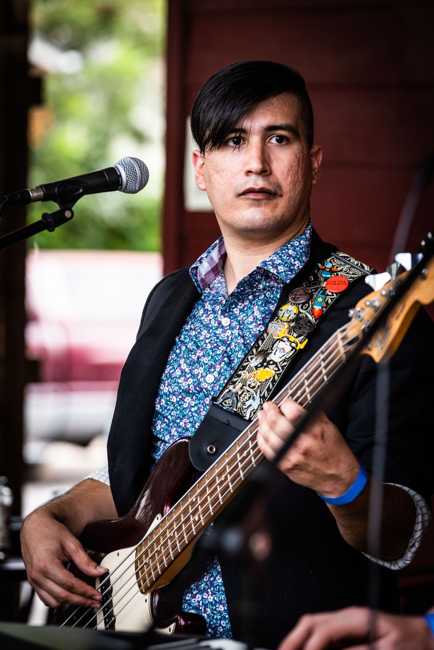 Bass guitarist in floral patterned shirt and black jacket performs with decorated guitar strap.