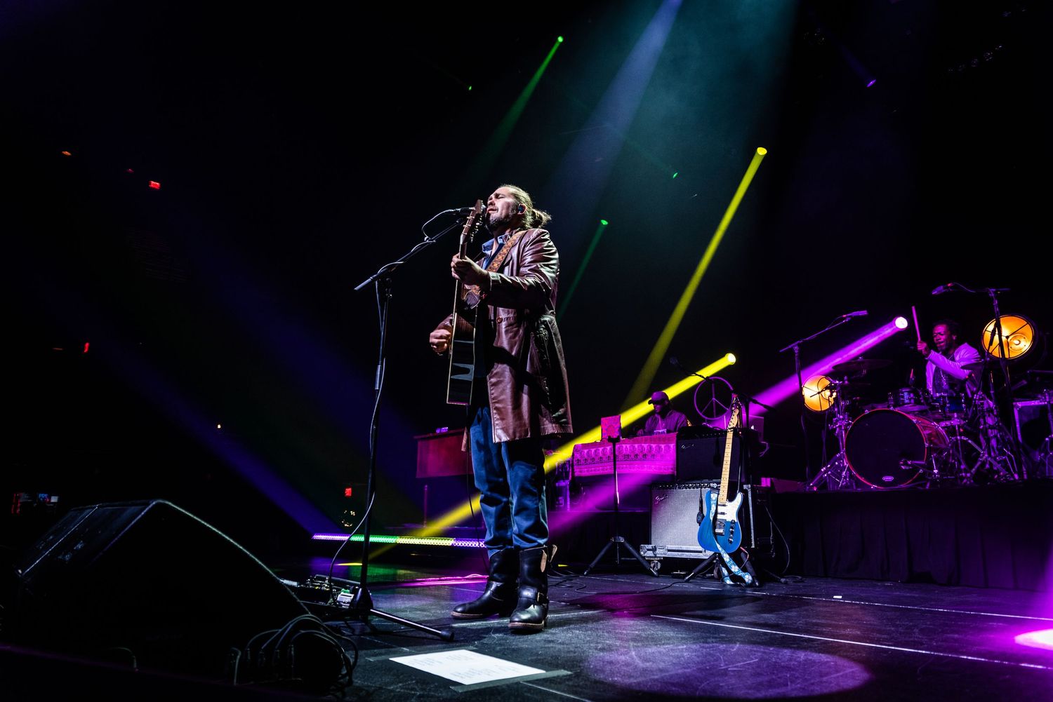 Solo artist performs on illuminated stage with colorful lighting and drum kit visible in background.