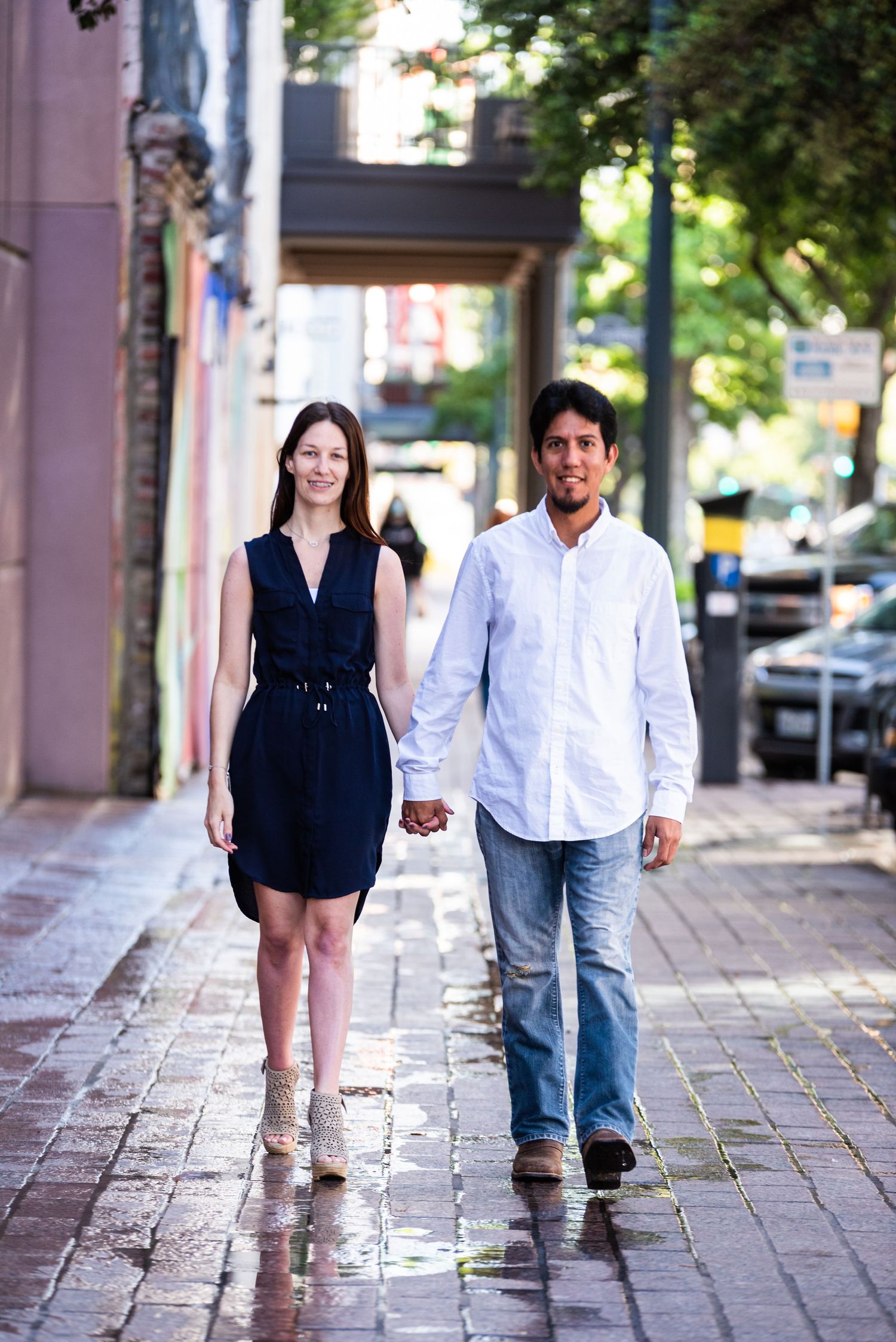 A couple holding hands while walking down a wet cobblestone street.