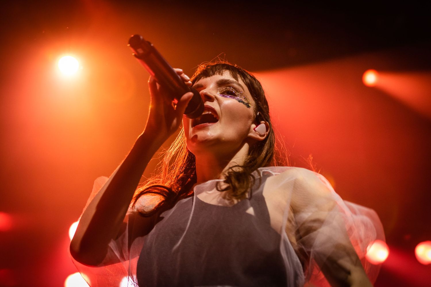 Concert performance shot with orange lighting shows singer emotionally delivering vocals.