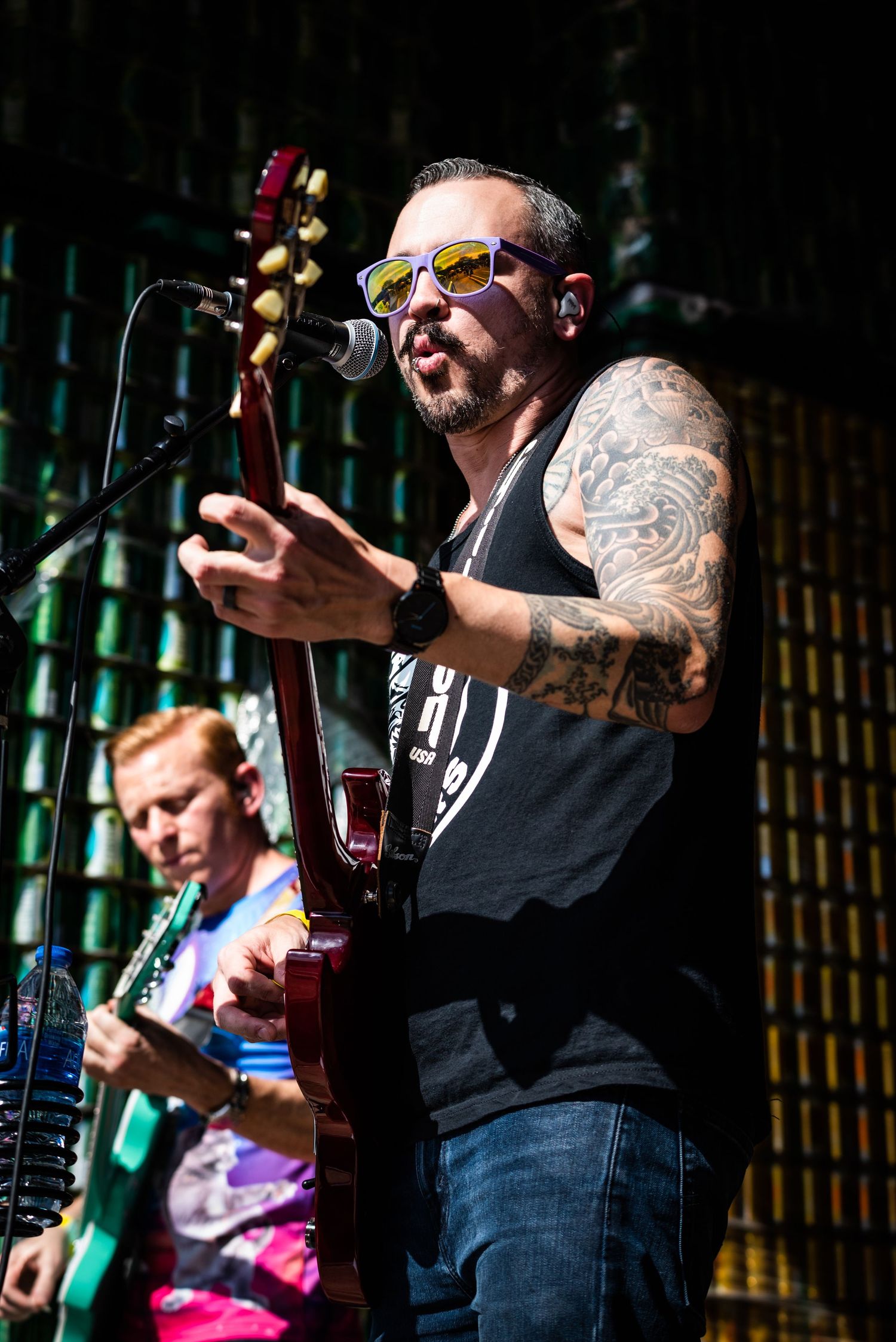 A tattooed musician sings and plays guitar during an energetic performance on stage.