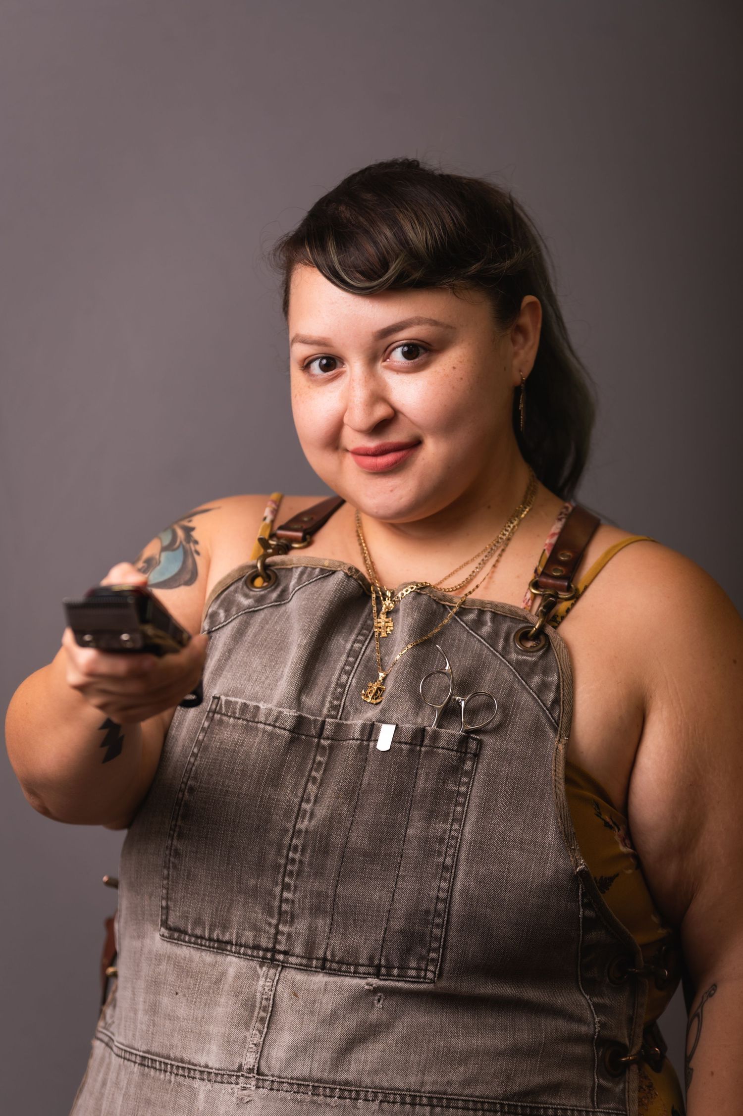 Casual portrait in denim overalls holding styling tool in studio setting.