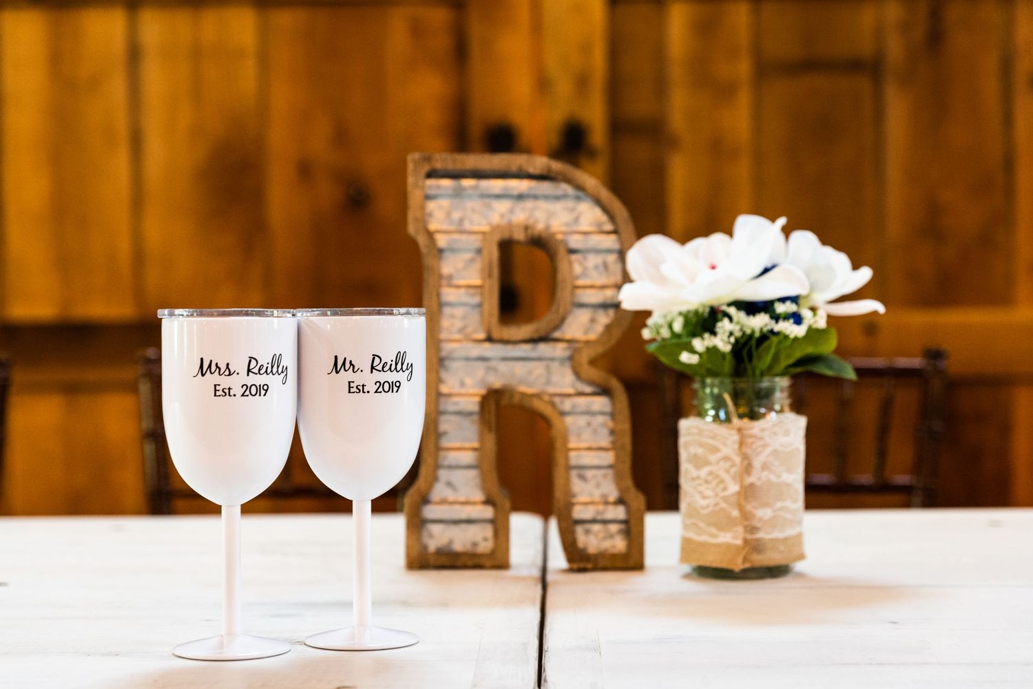 Two personalized wedding wine glasses sit beside a decorative letter R on a wooden table.