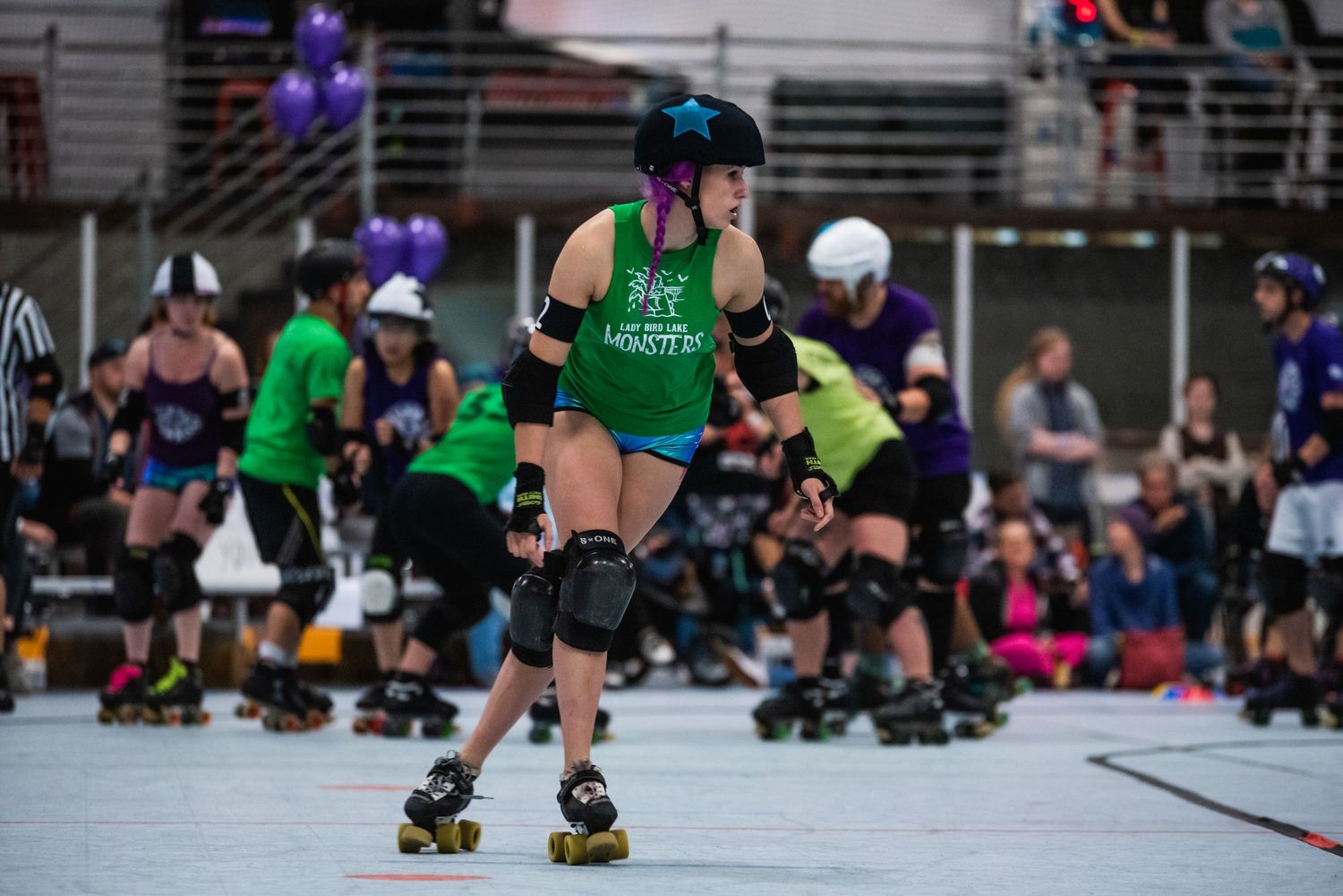 Roller derby athlete in green jersey and protective gear skating during competition.