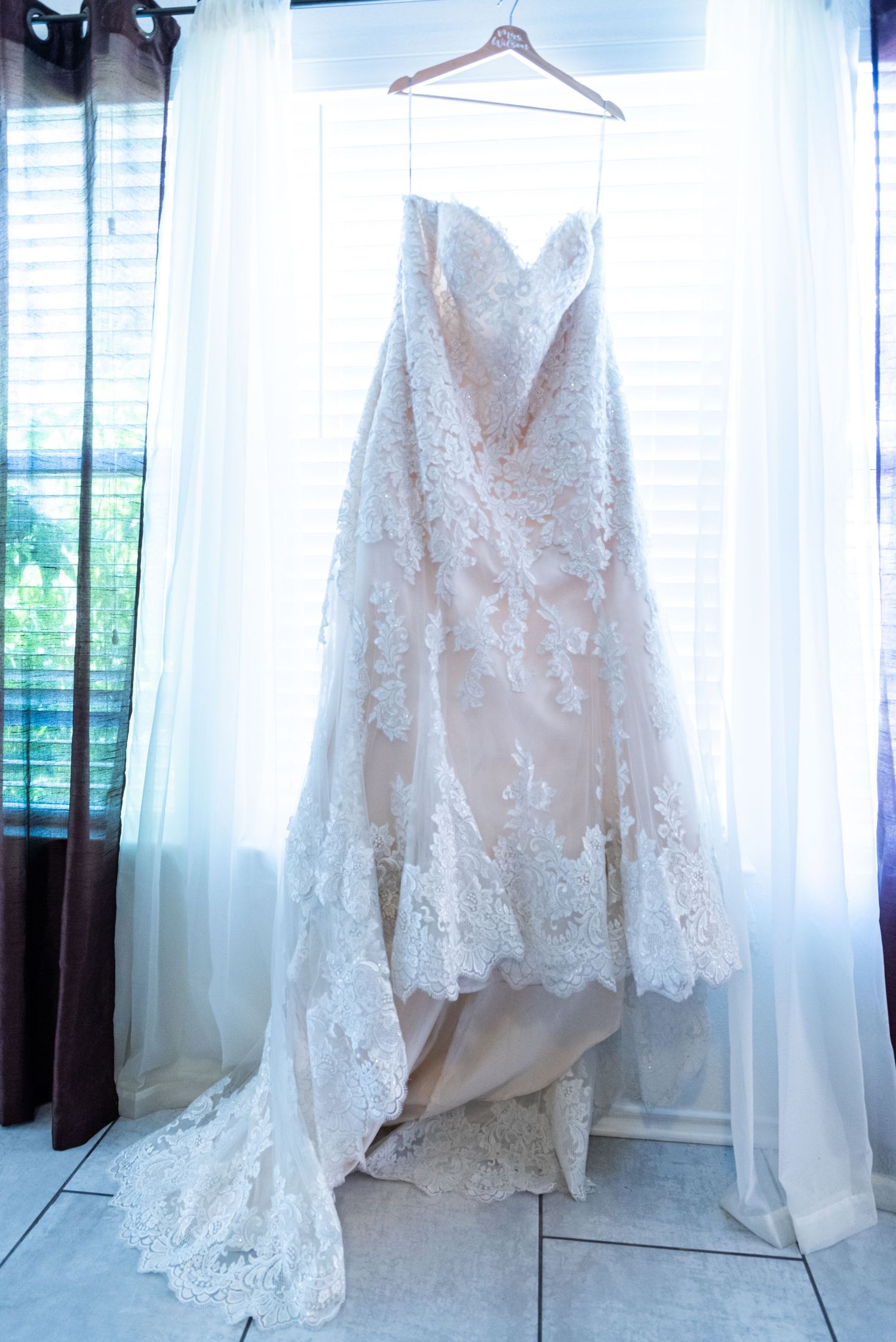 White lace wedding dress with sweetheart neckline hangs elegantly against window light.