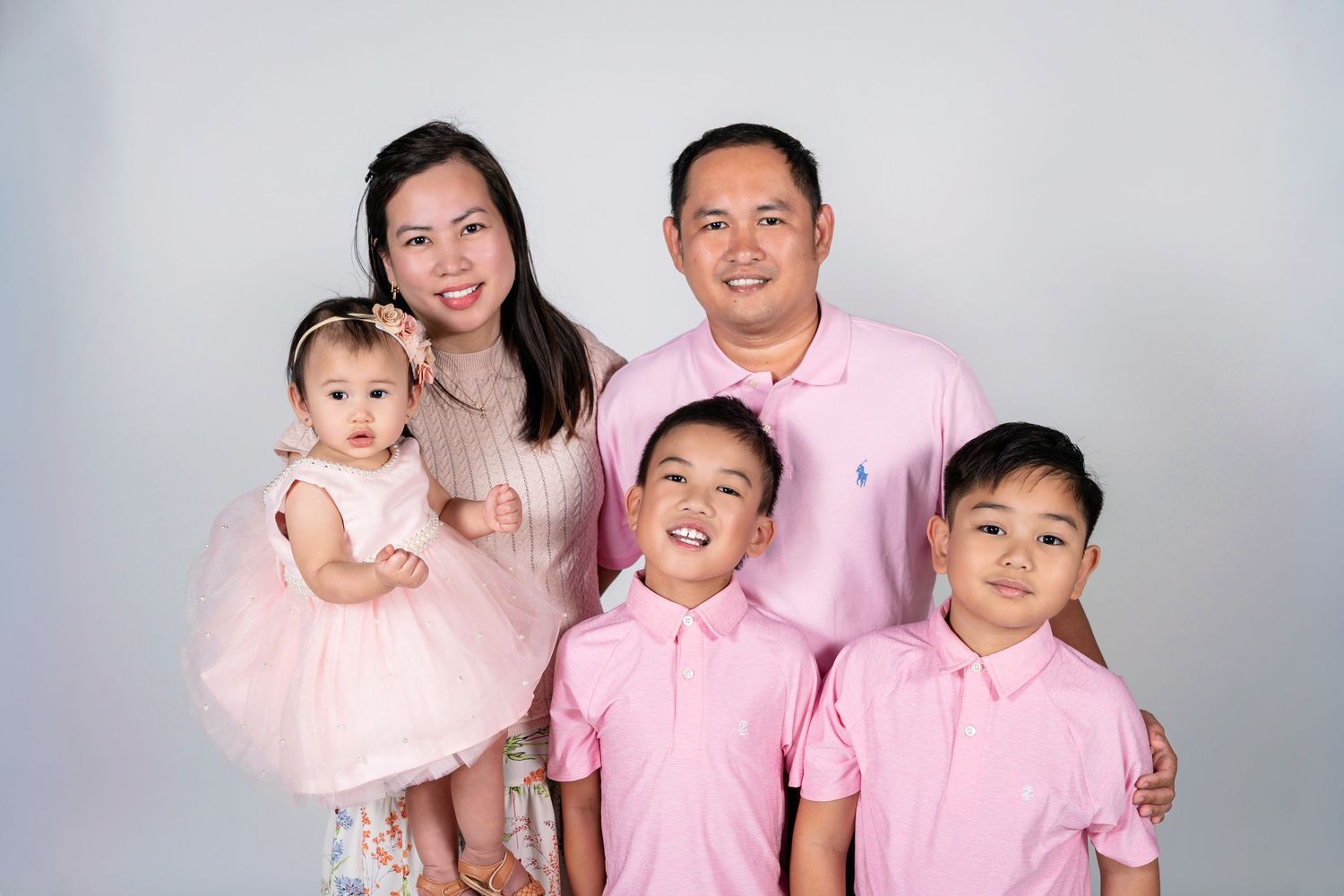 A happy Asian family of five wearing matching pink outfits poses together in a professional studio portrait.