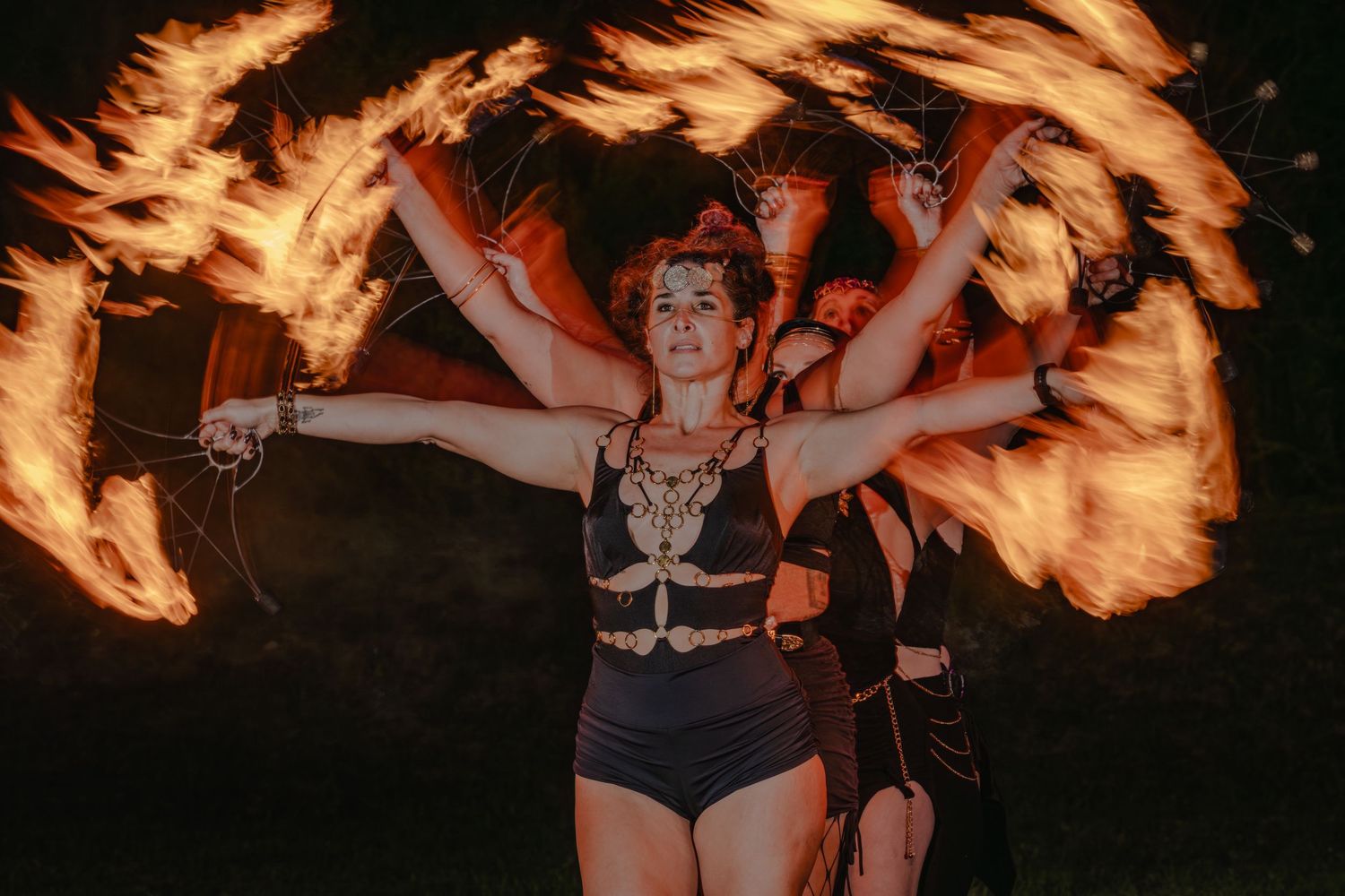 Fire dancer performs with swirling flames at night, wearing costume with arms raised in dramatic pose.