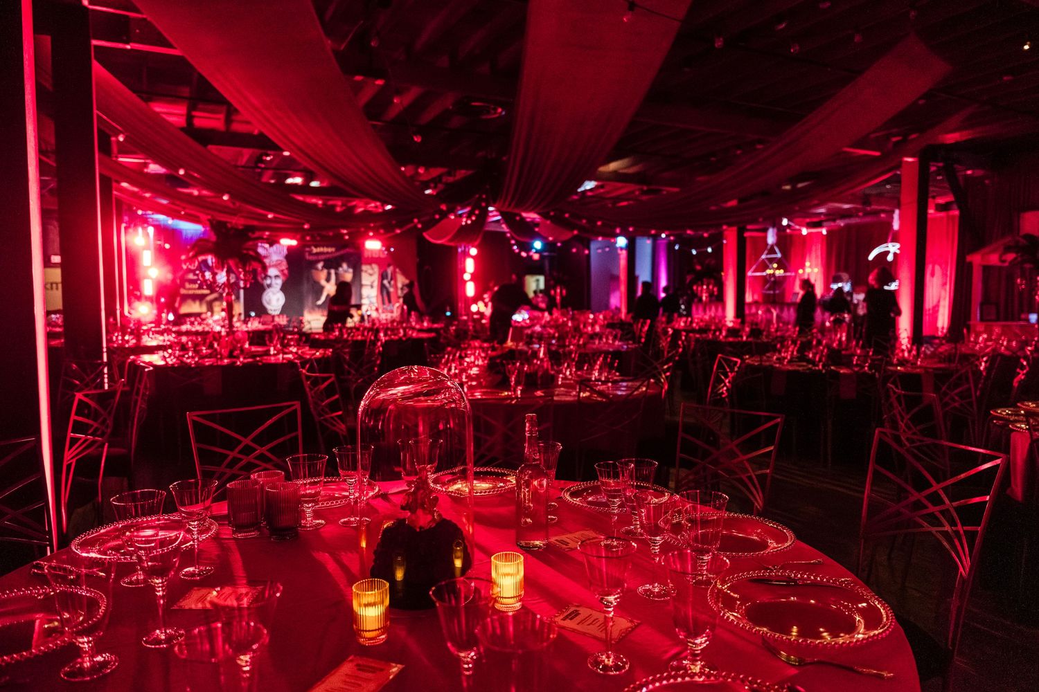 Elegant banquet hall bathed in dramatic red lighting with round tables set for a formal dinner event.