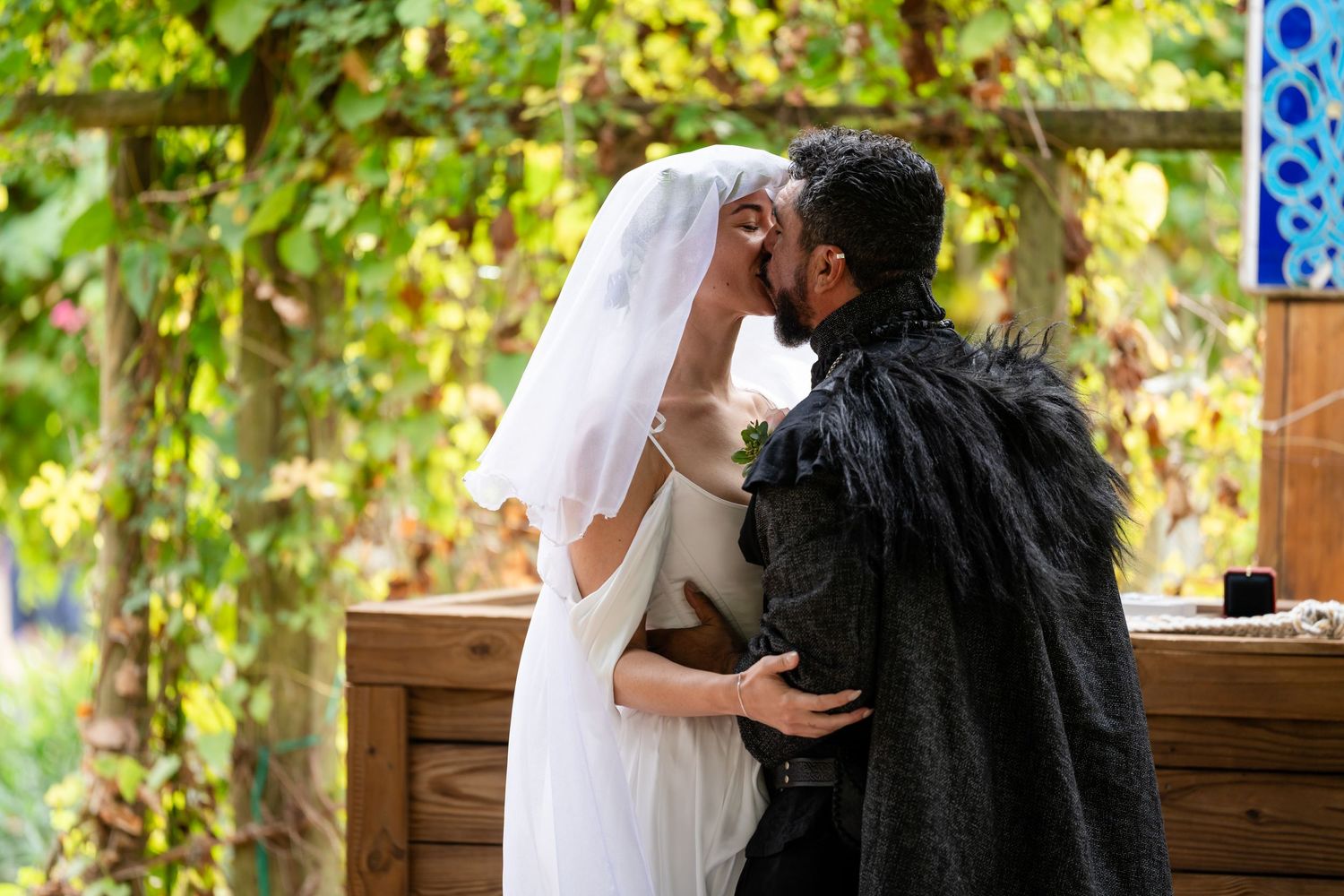 A romantic couple shares tender moments in a rustic outdoor setting surrounded by lush greenery and natural light.