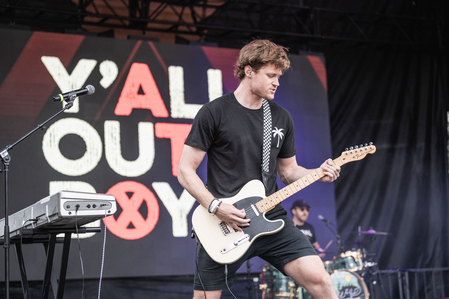 A musician performs on stage with an electric guitar in front of a large 'Fall Out Boy' backdrop during a concert.