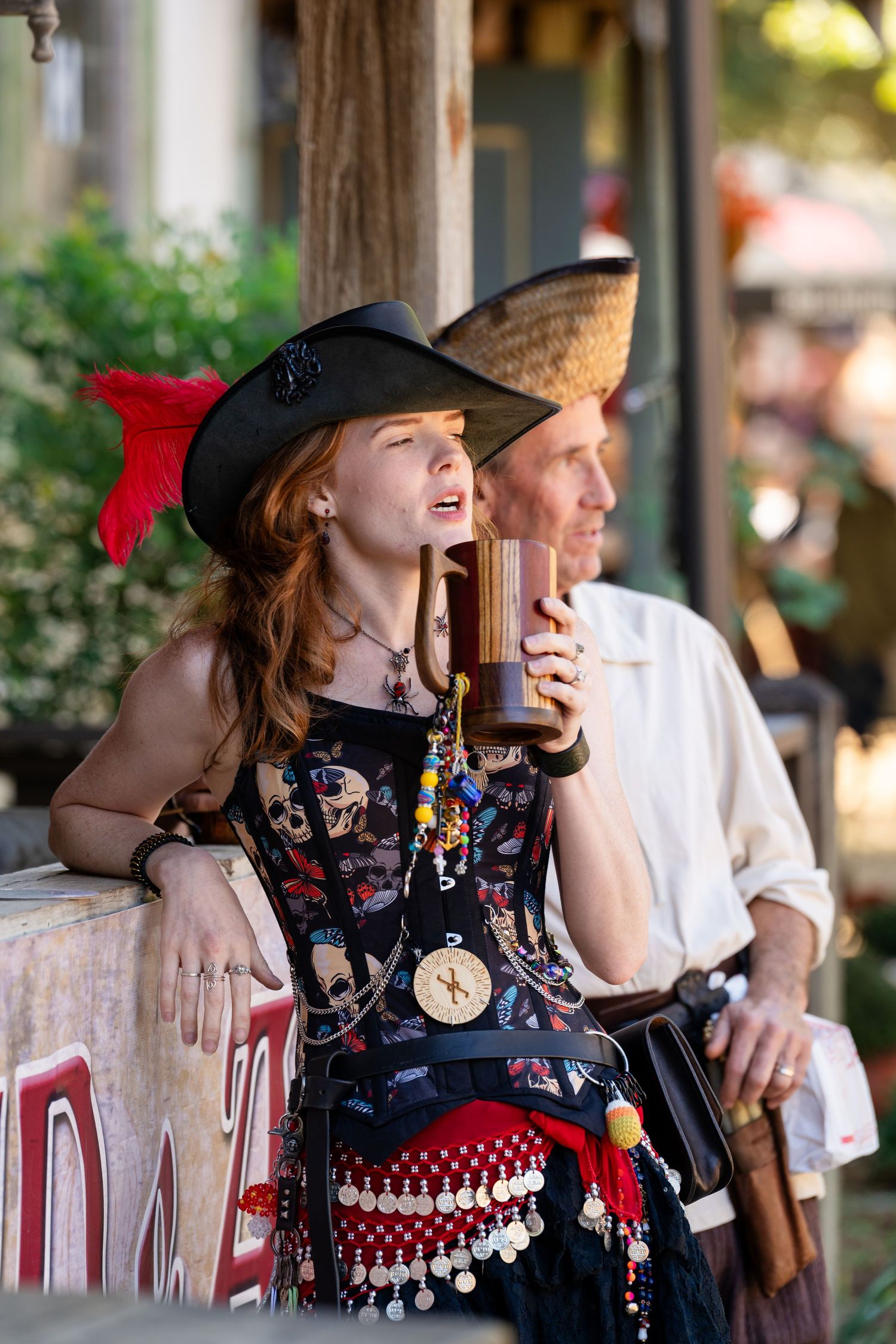 A person in a black patterned dress and red hat laughs while sitting at an outdoor cafe table.