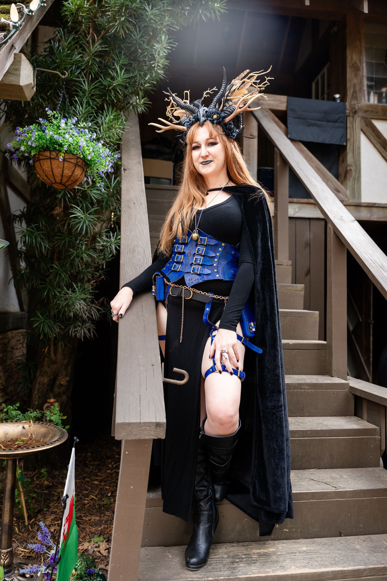 A maternity photoshoot on wooden stairs features a black dress and blue belly art in a creative outdoor setting.