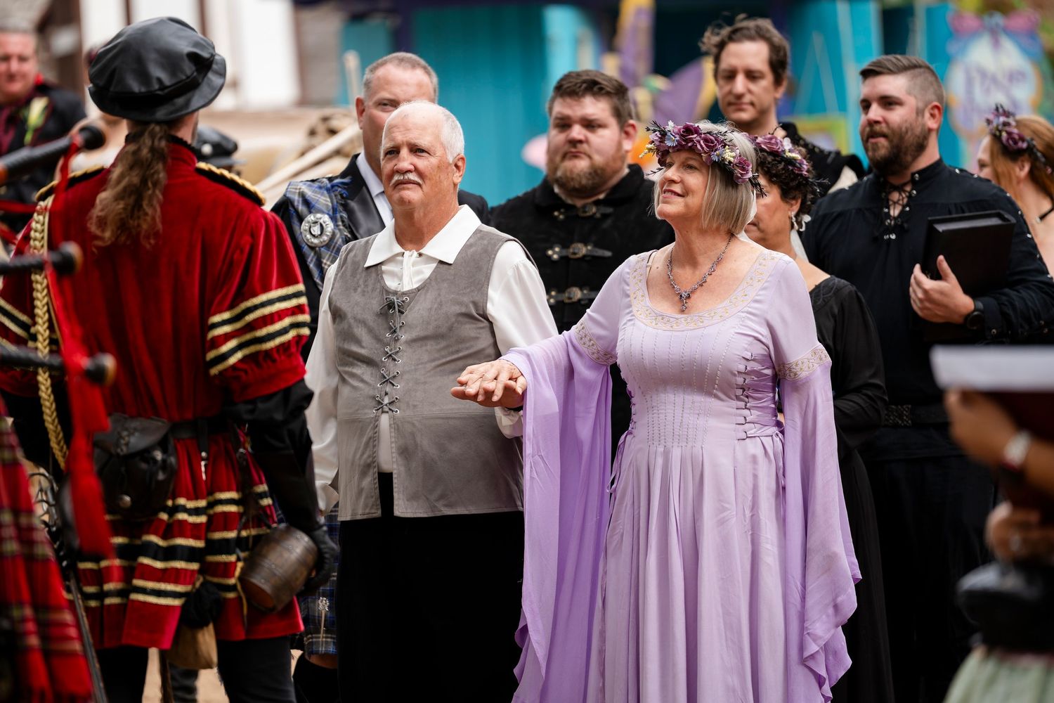 A person in a flowing lavender gown poses on a red carpet surrounded by photographers and onlookers.