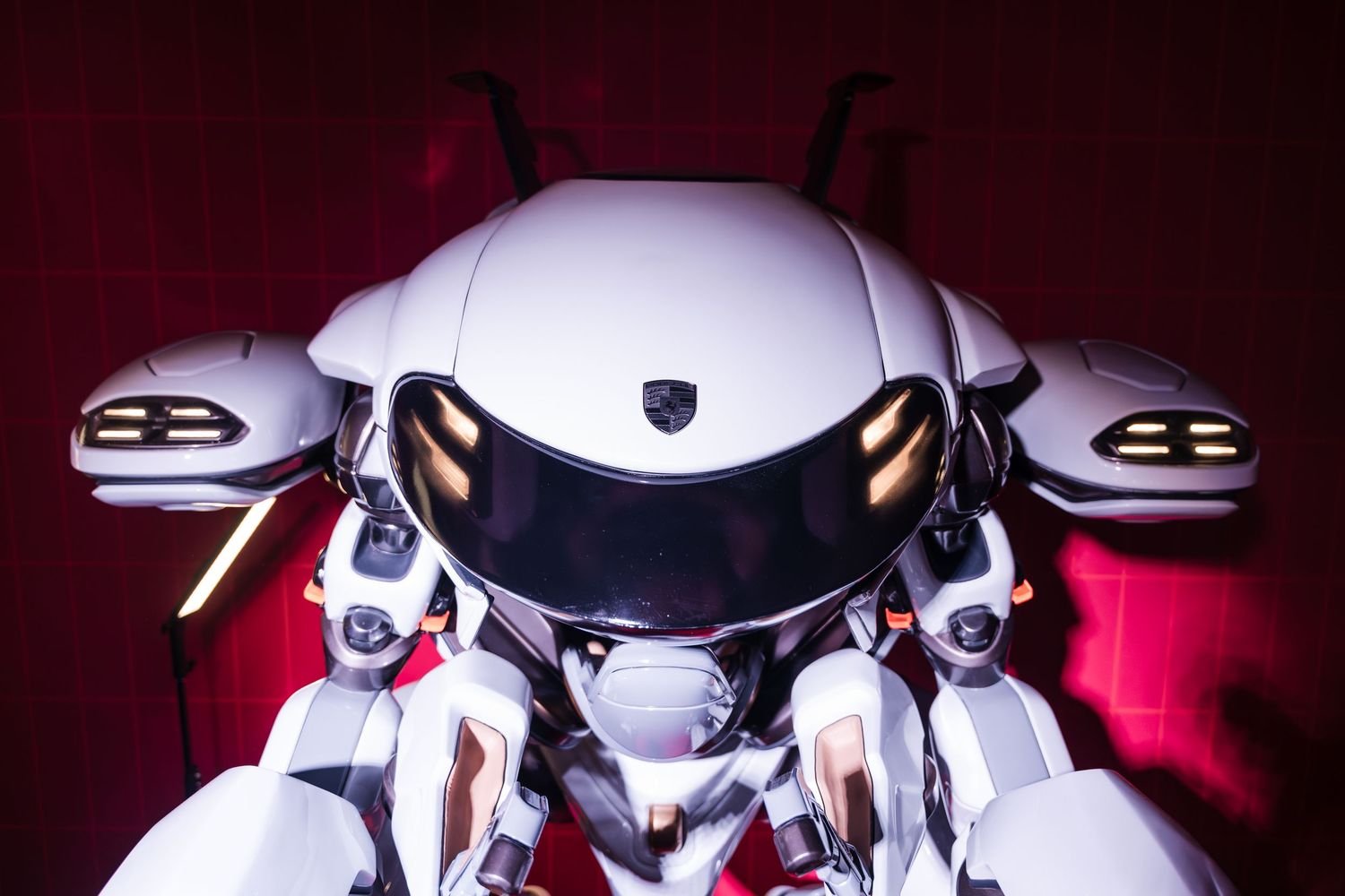 Sleek white motorcycle helmet with reflective visor displayed against dark background with dramatic red lighting.