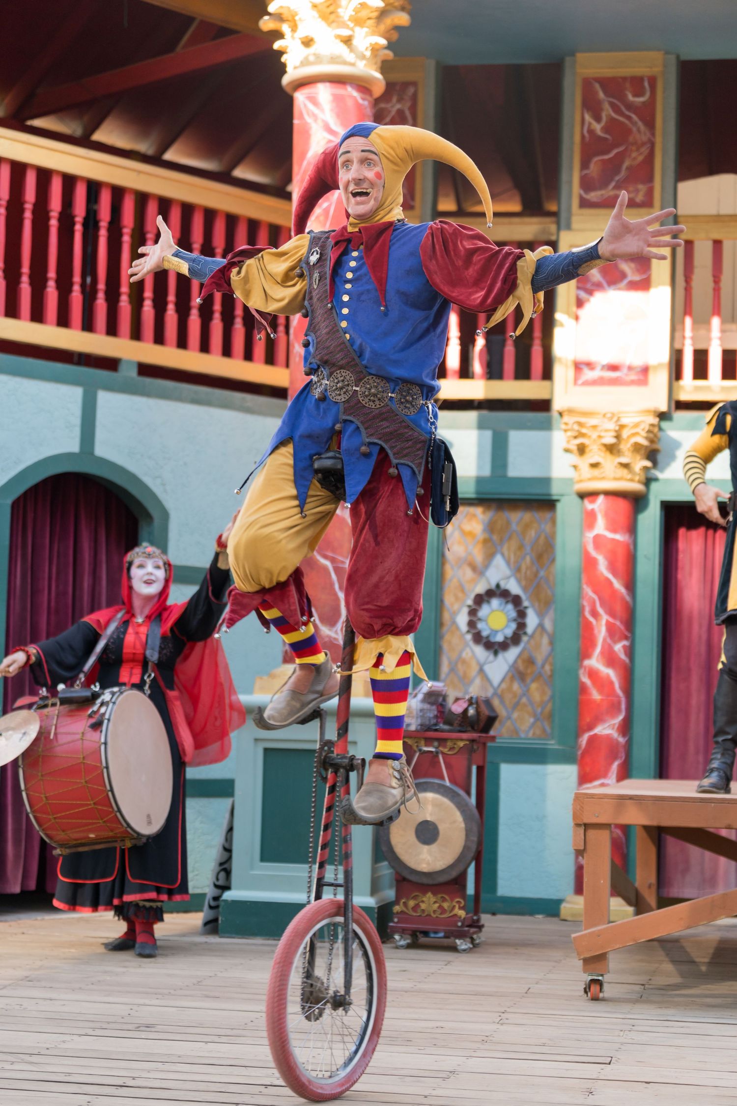 Performers in medieval costumes ride unicycles and play instruments during a Renaissance fair entertainment show.