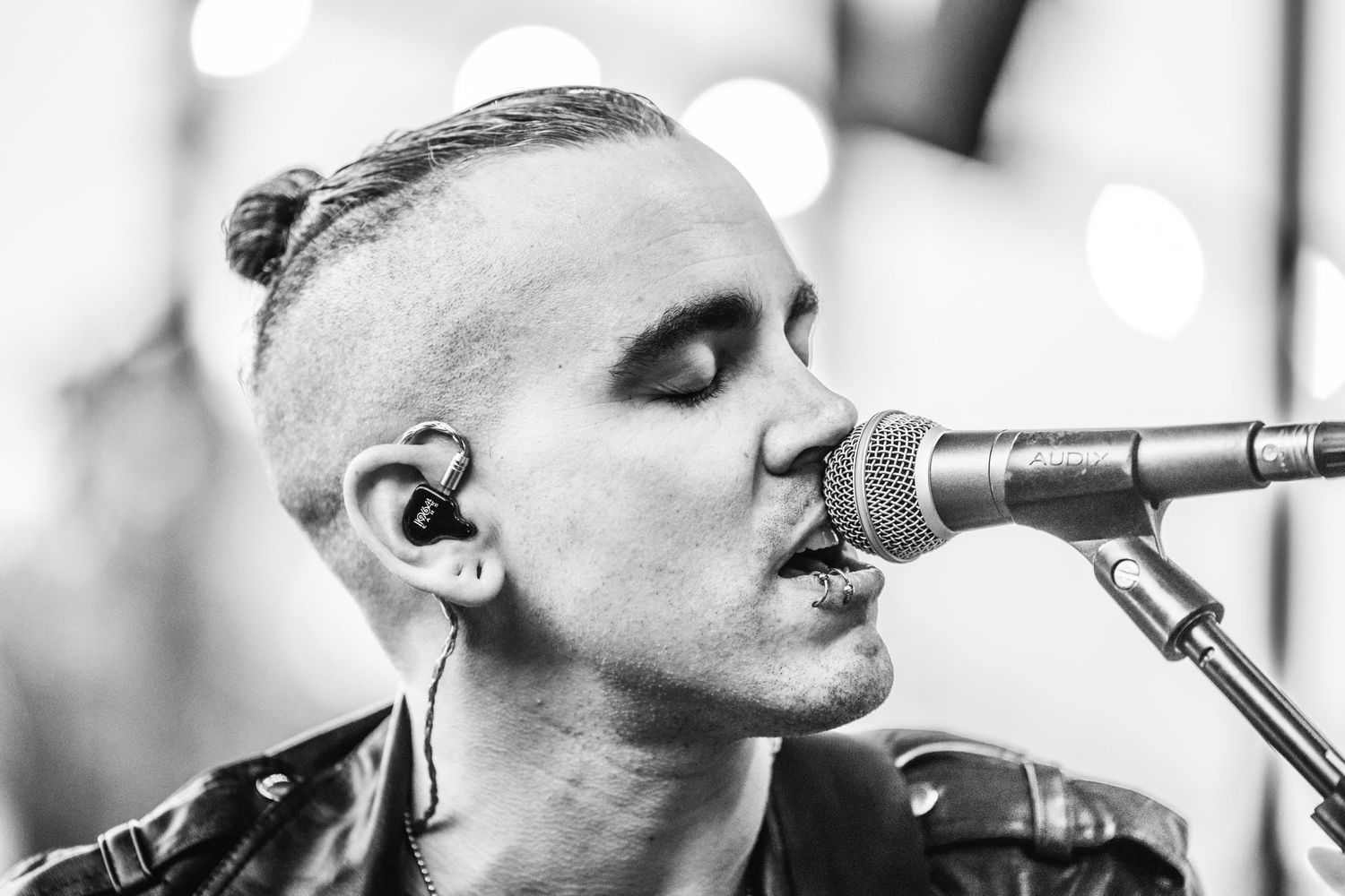 A black and white photo shows performers singing into vintage microphones on stage during a live performance.