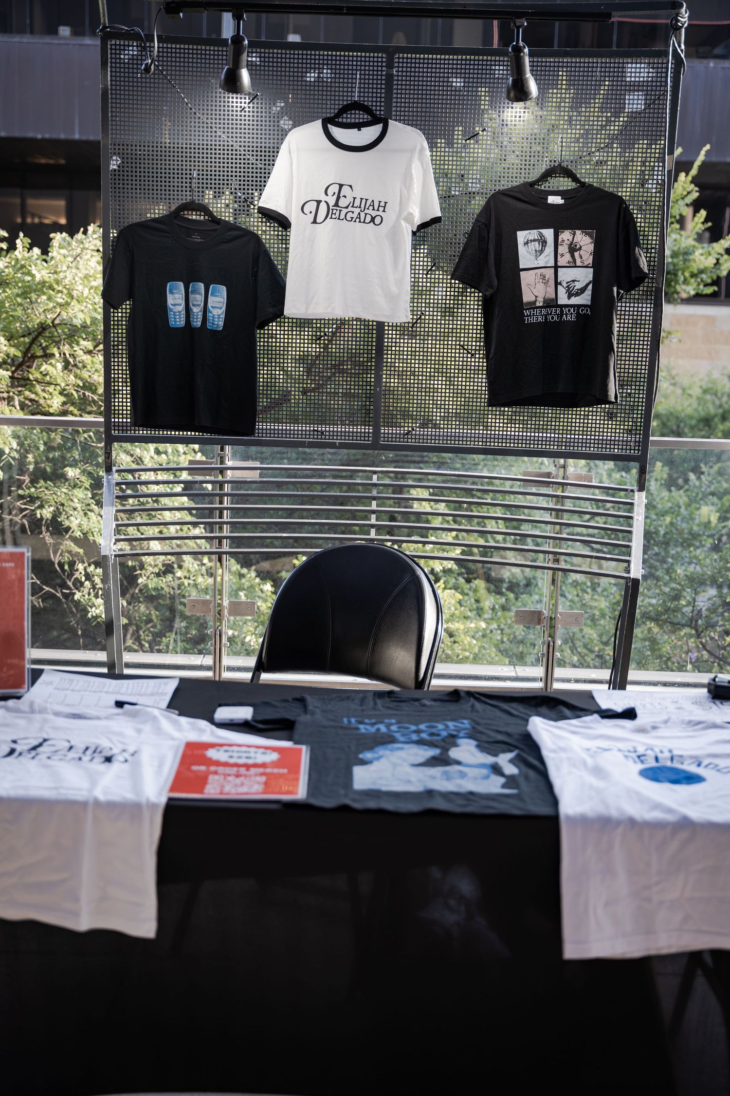 Merchandise booth displaying black and white t-shirts on a rack with additional shirts laid out on a table.