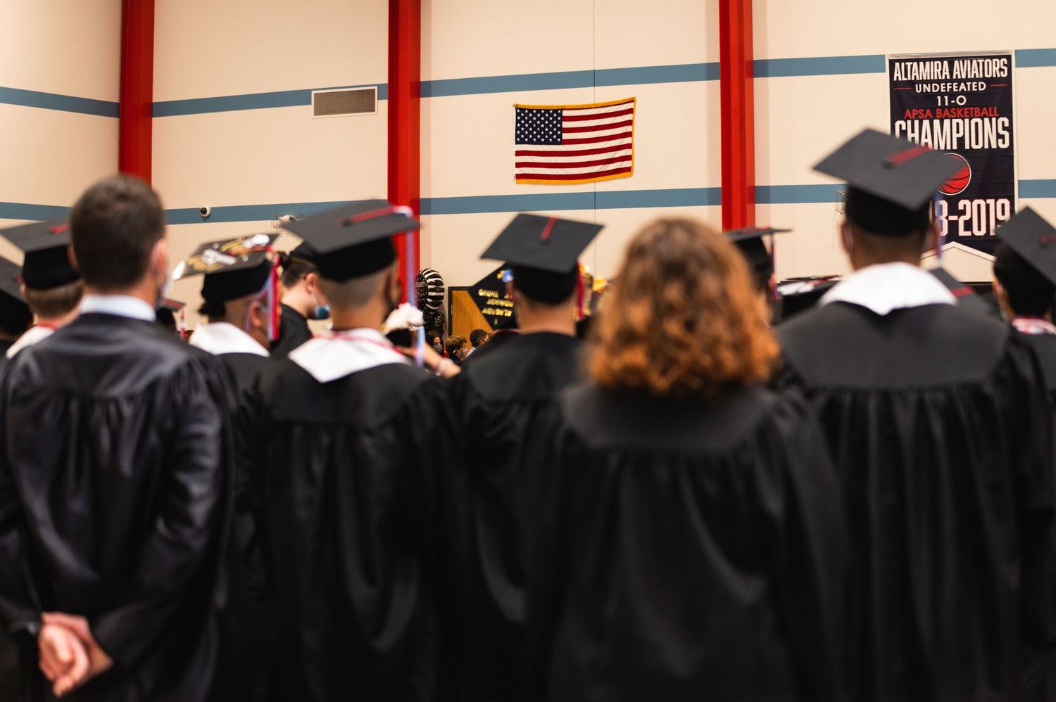 Graduates in black regalia face American flag during ceremony.