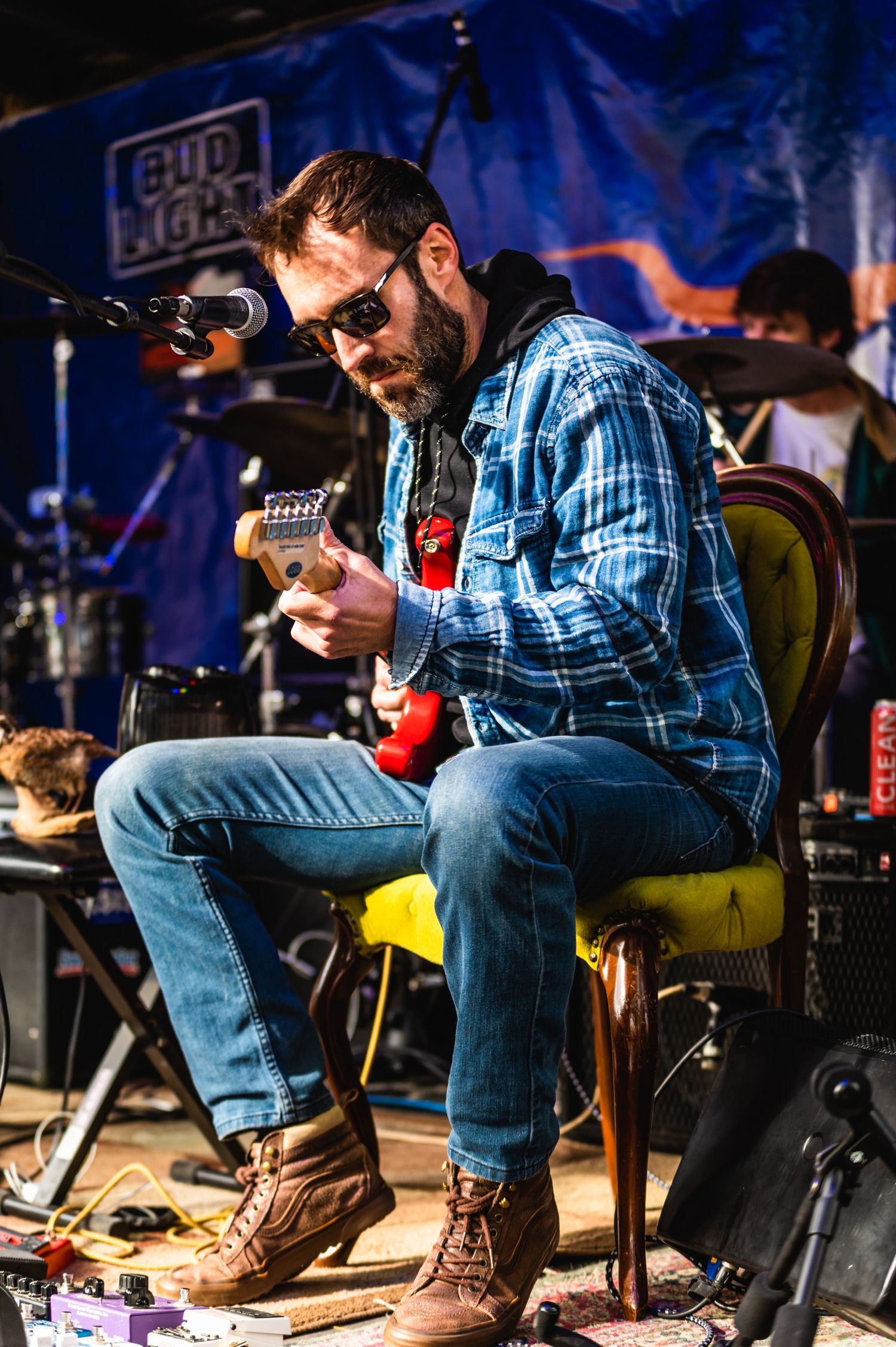 Musician in plaid shirt and sunglasses performs on stage with Bud Light banner.