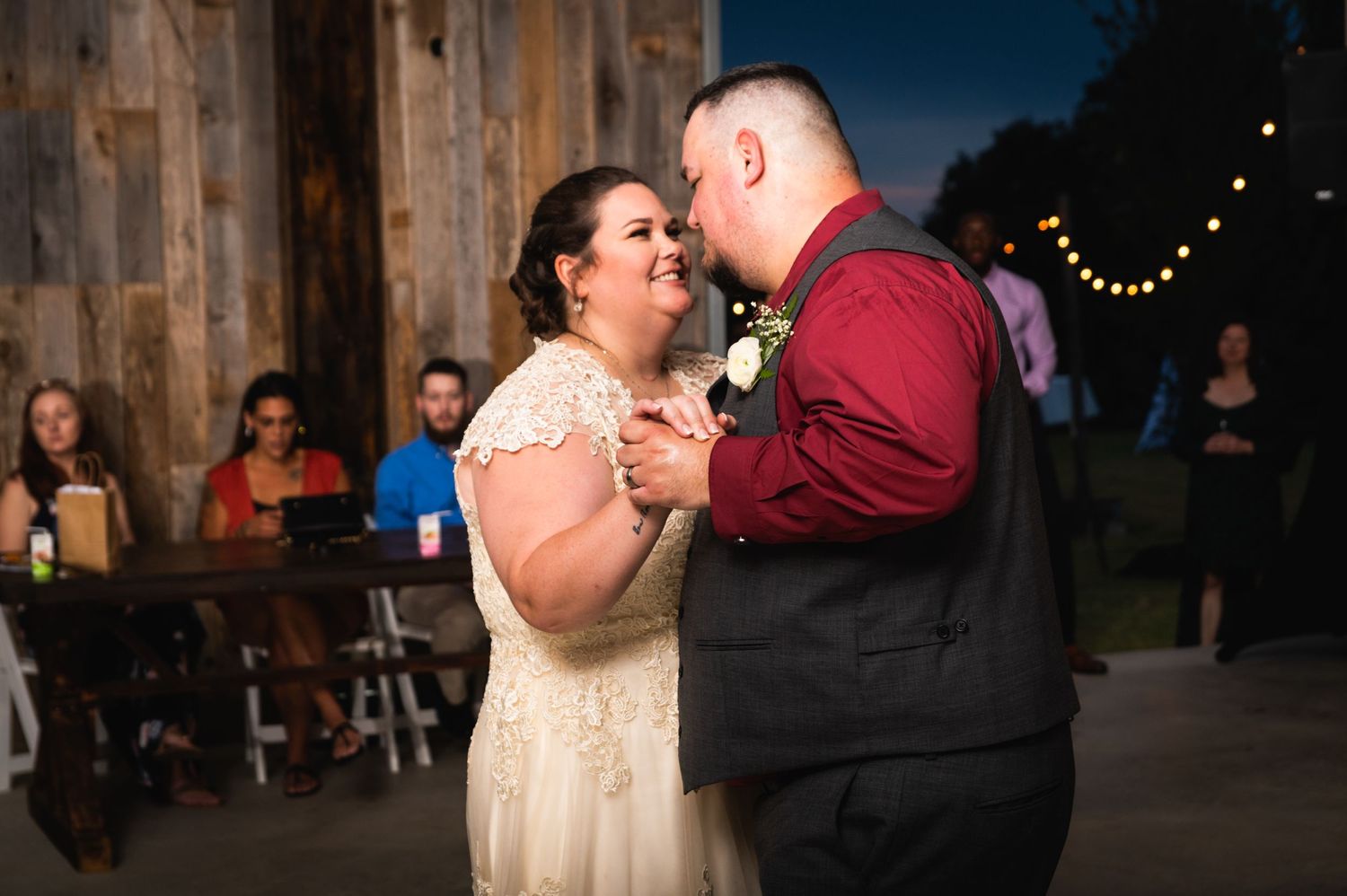 A couple shares a close dance together at their wedding reception with string lights in the background.