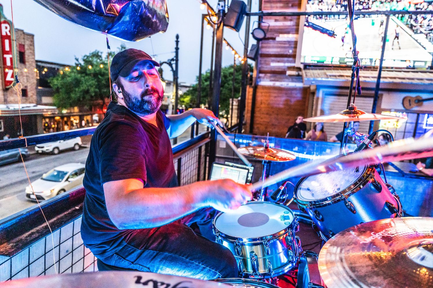 Drummer performing at outdoor venue with dramatic blue and red lighting.