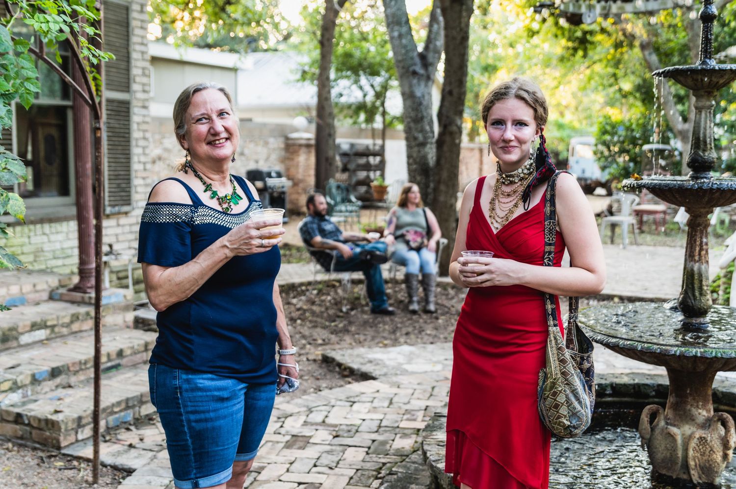 Two people enjoy drinks at an outdoor garden party with stone decor.
