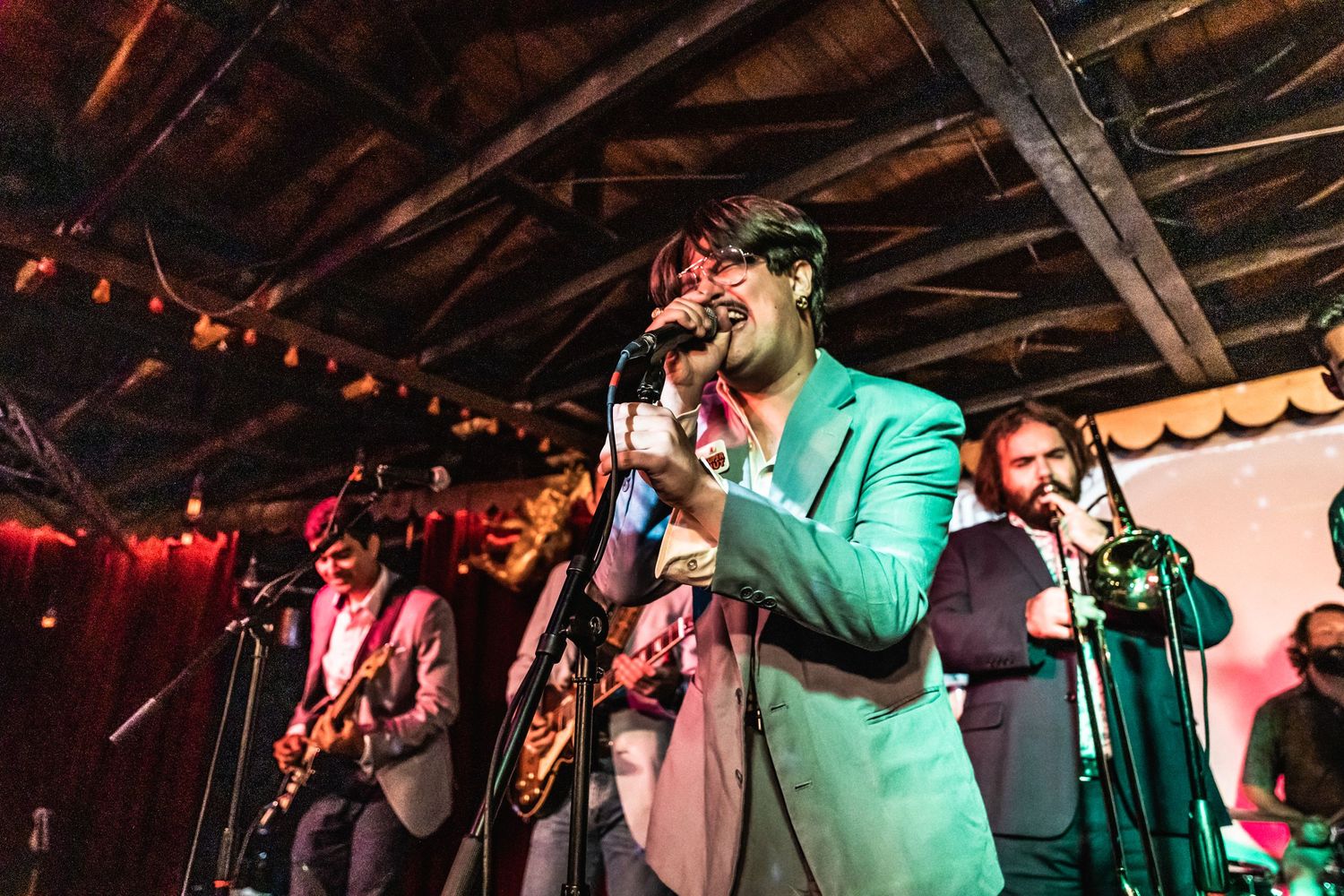 Band members performing on stage with a singer in a mint green blazer under dramatic lighting.