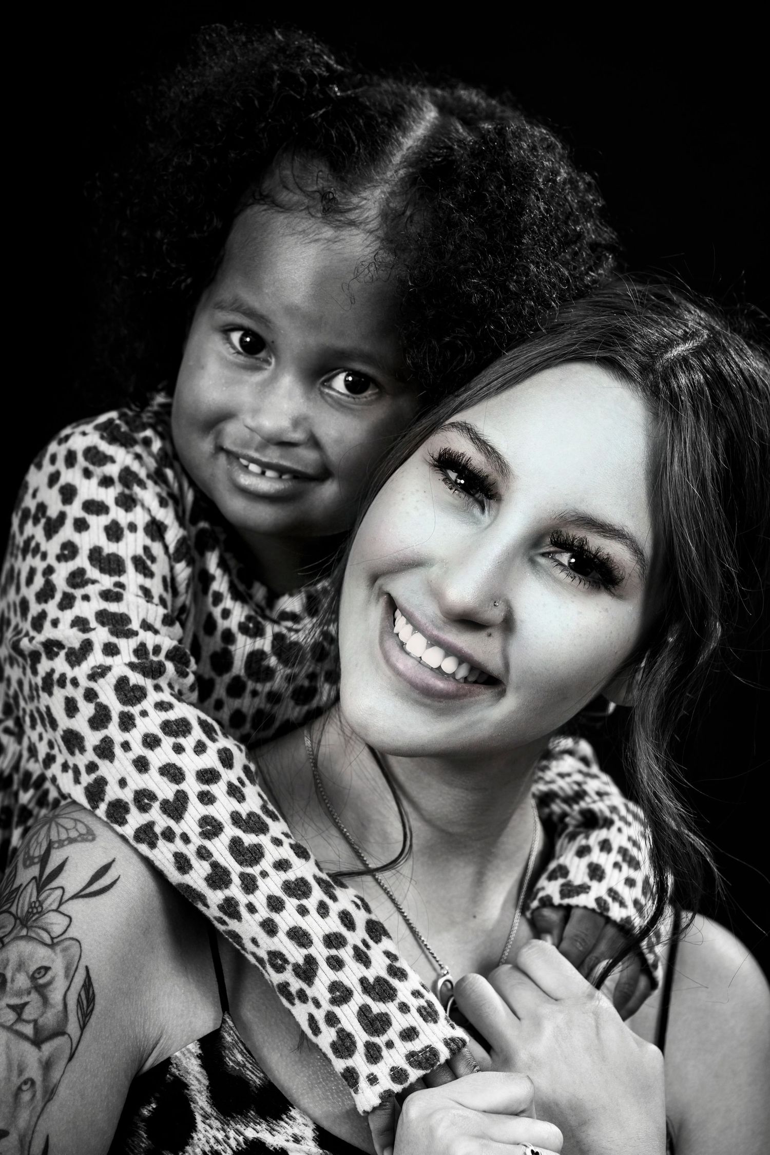 Black and white portrait showing joyful embrace between child and woman in matching leopard print.