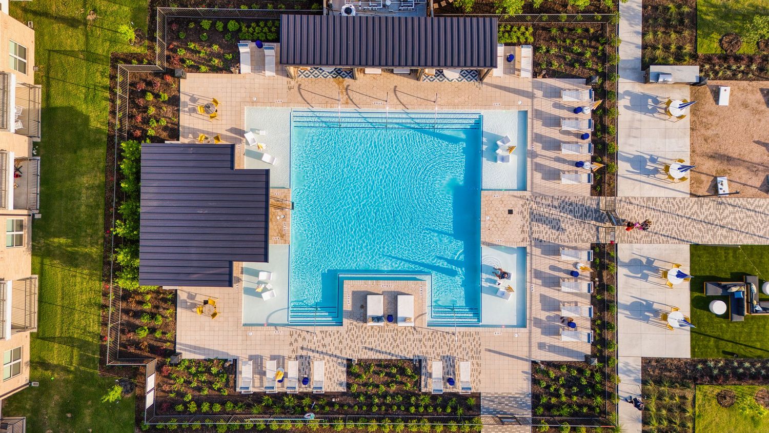 Aerial view of modern swimming pool with lounge chairs and landscaping at apartment complex.