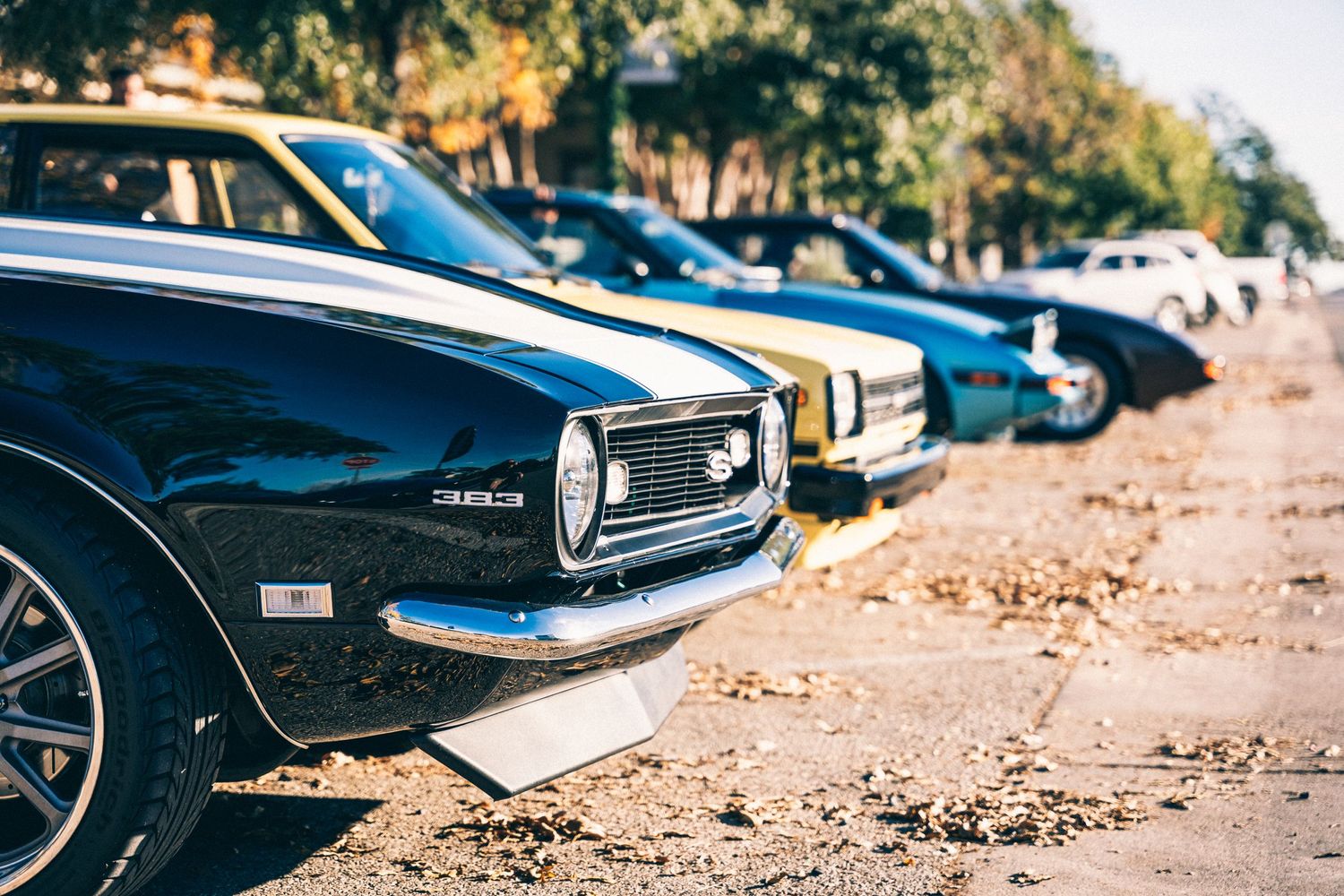 Classic muscle cars lined up in a row showing their front grilles and bumpers.