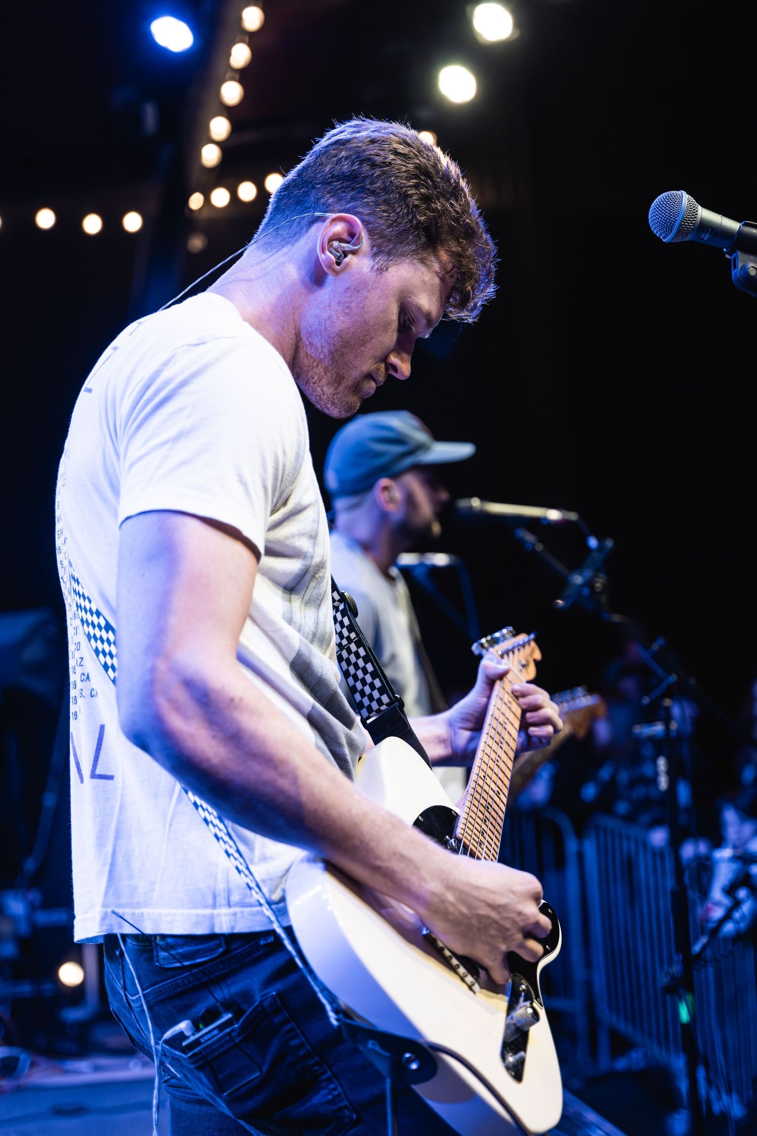 Guitarist in white t-shirt playing electric guitar under stage lights.