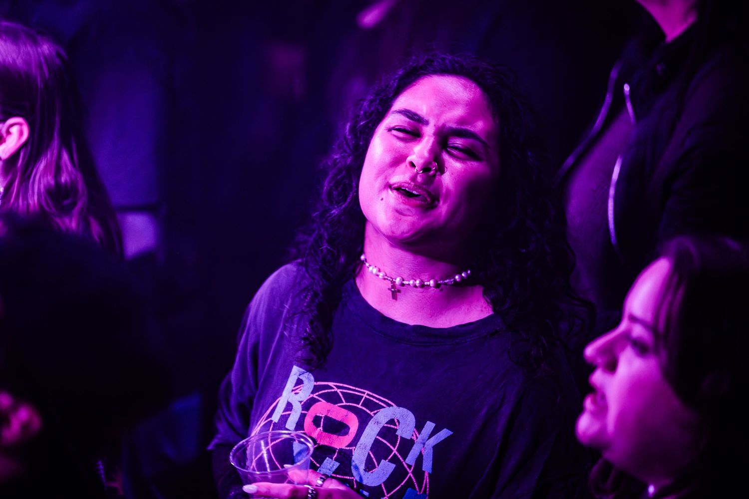 Concert attendee in rock t-shirt enjoying music under purple lighting.