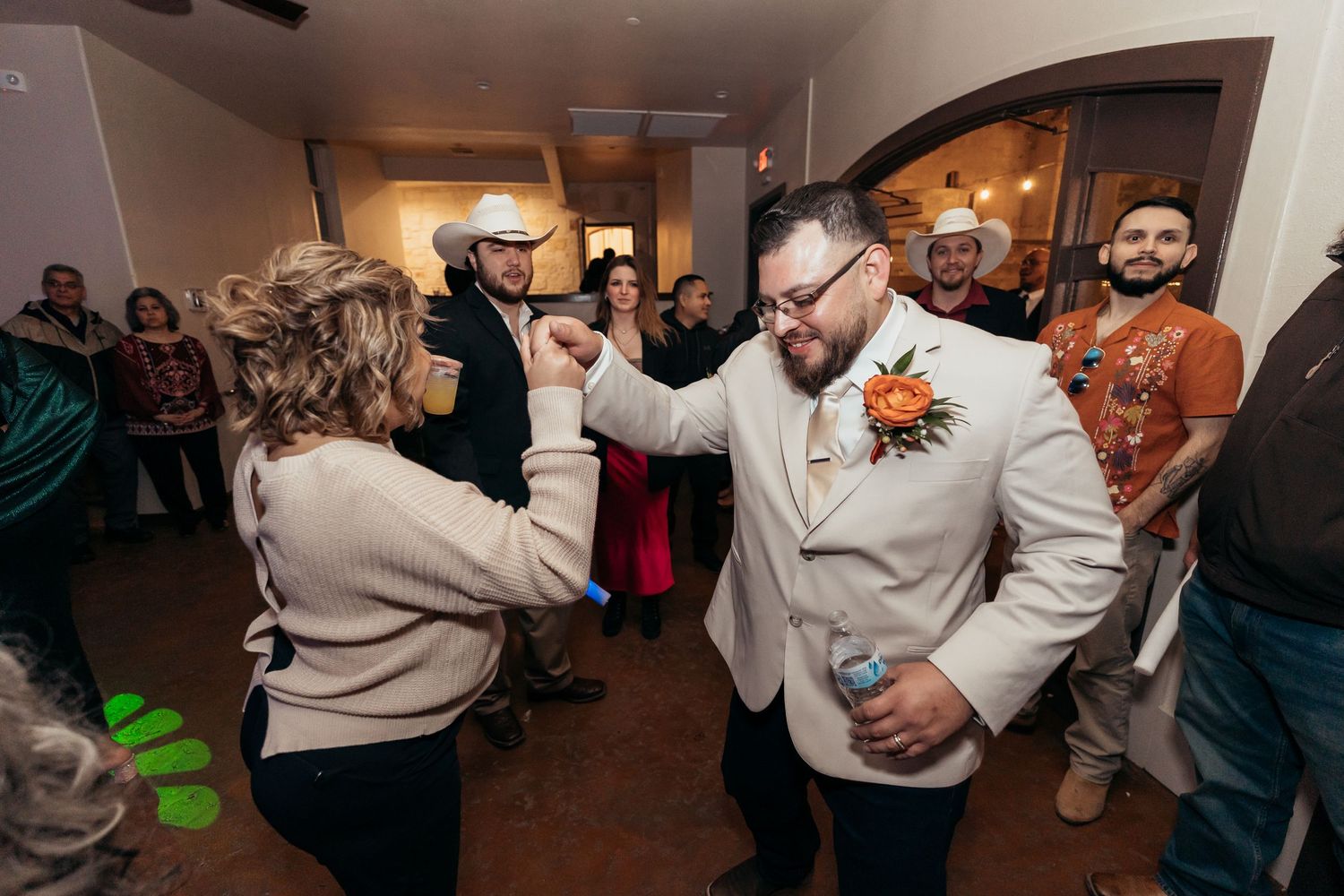 Wedding guests dancing and celebrating in an indoor venue with arched doorways.