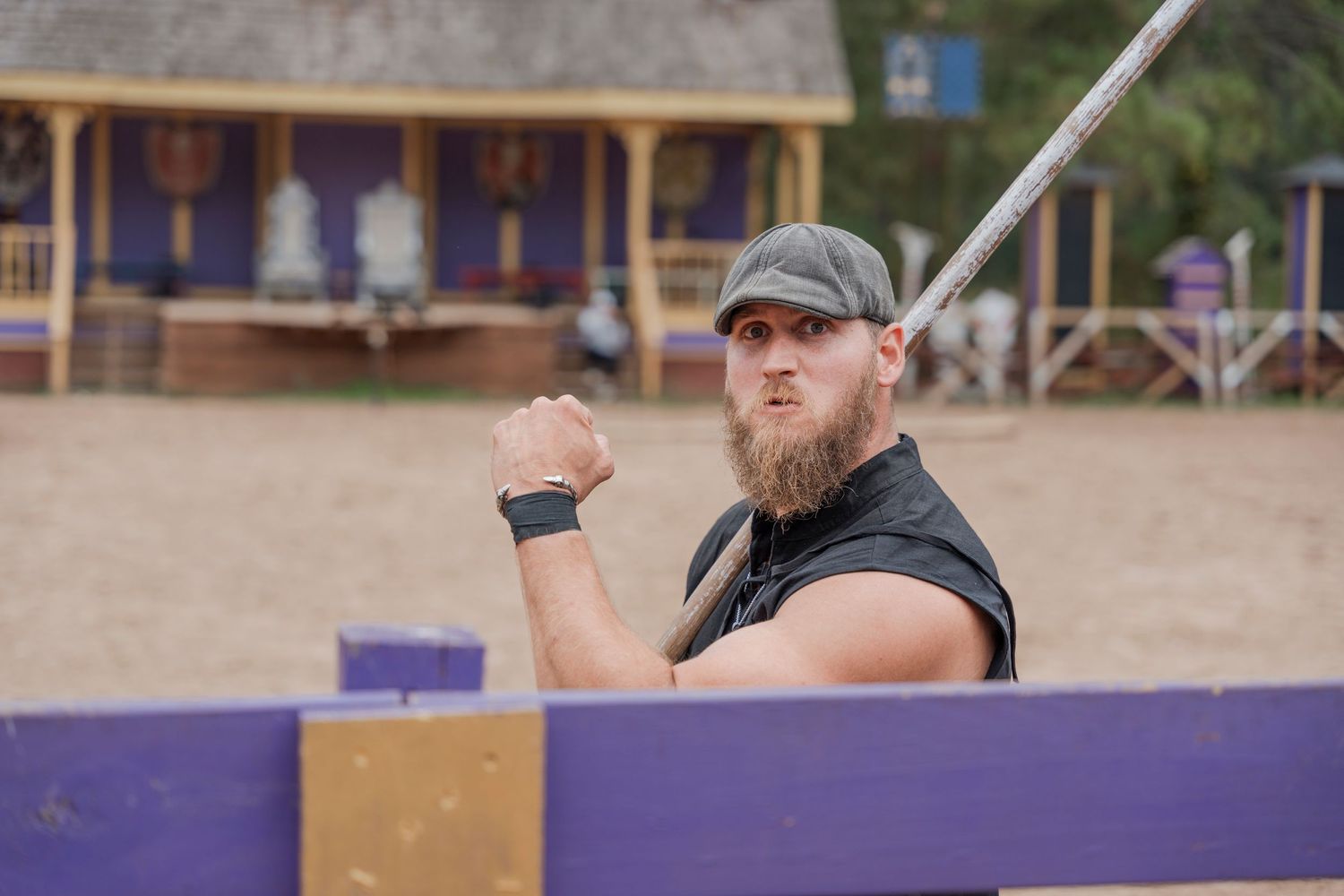 Bearded performer in black vest raising fist at outdoor renaissance festival.