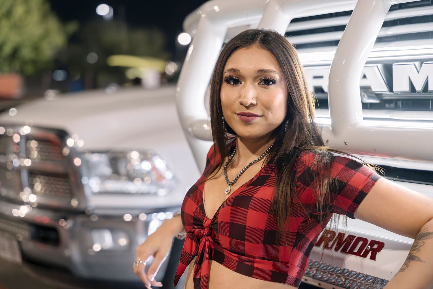Red plaid crop top styled against white RAM truck grille at car show.