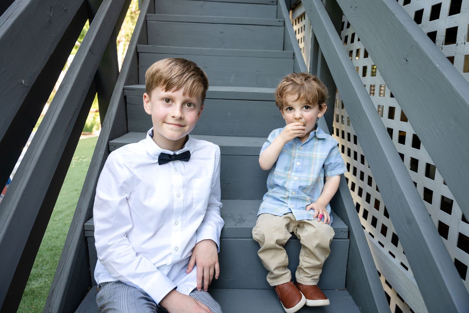Two young boys in formal attire sitting on gray outdoor stairs.