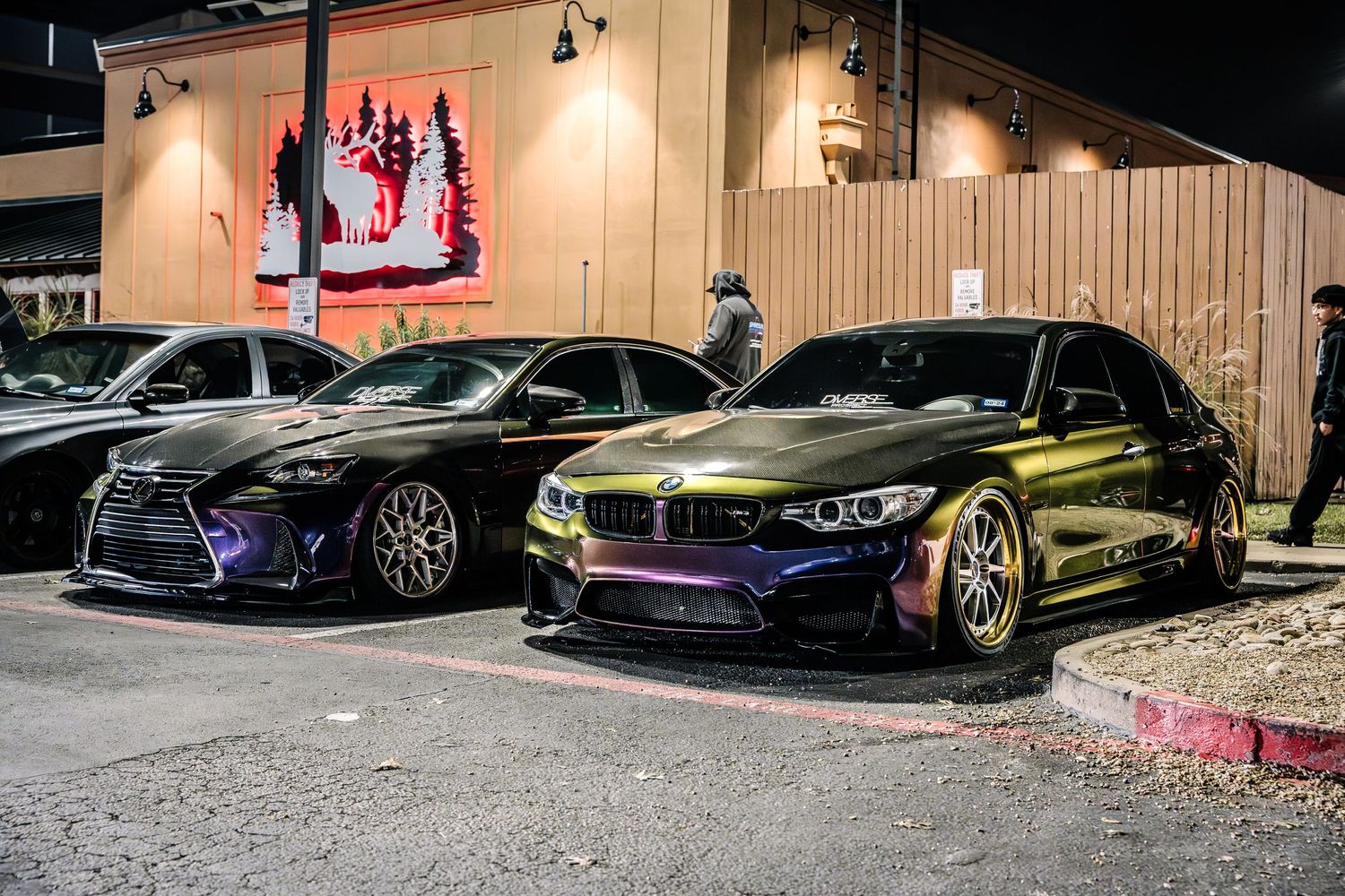 BMW performance vehicles with custom modifications parked at night showing colorful paint finishes.