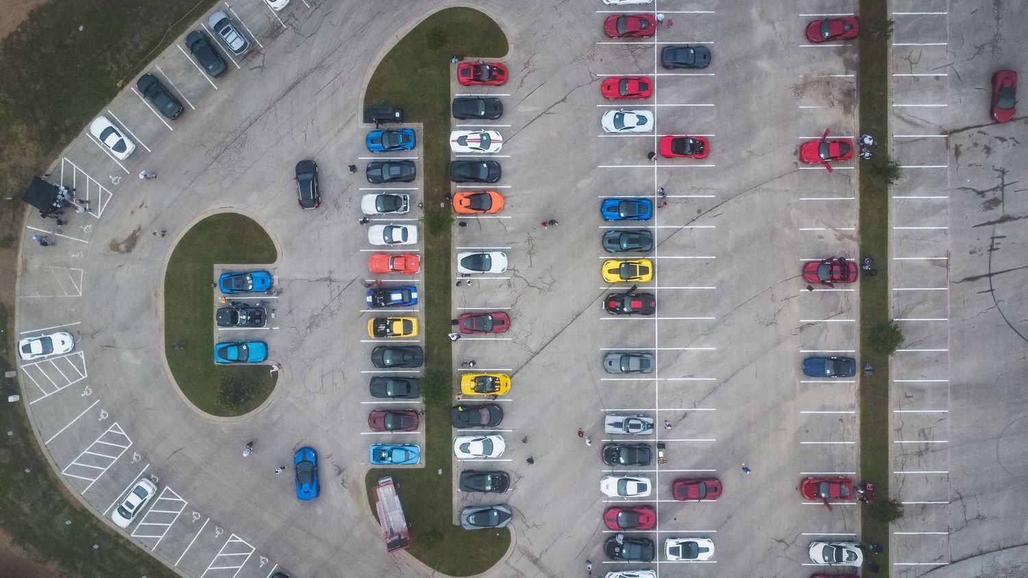 Bird's eye view of vehicles neatly organized in curved rows at car meet parking lot.