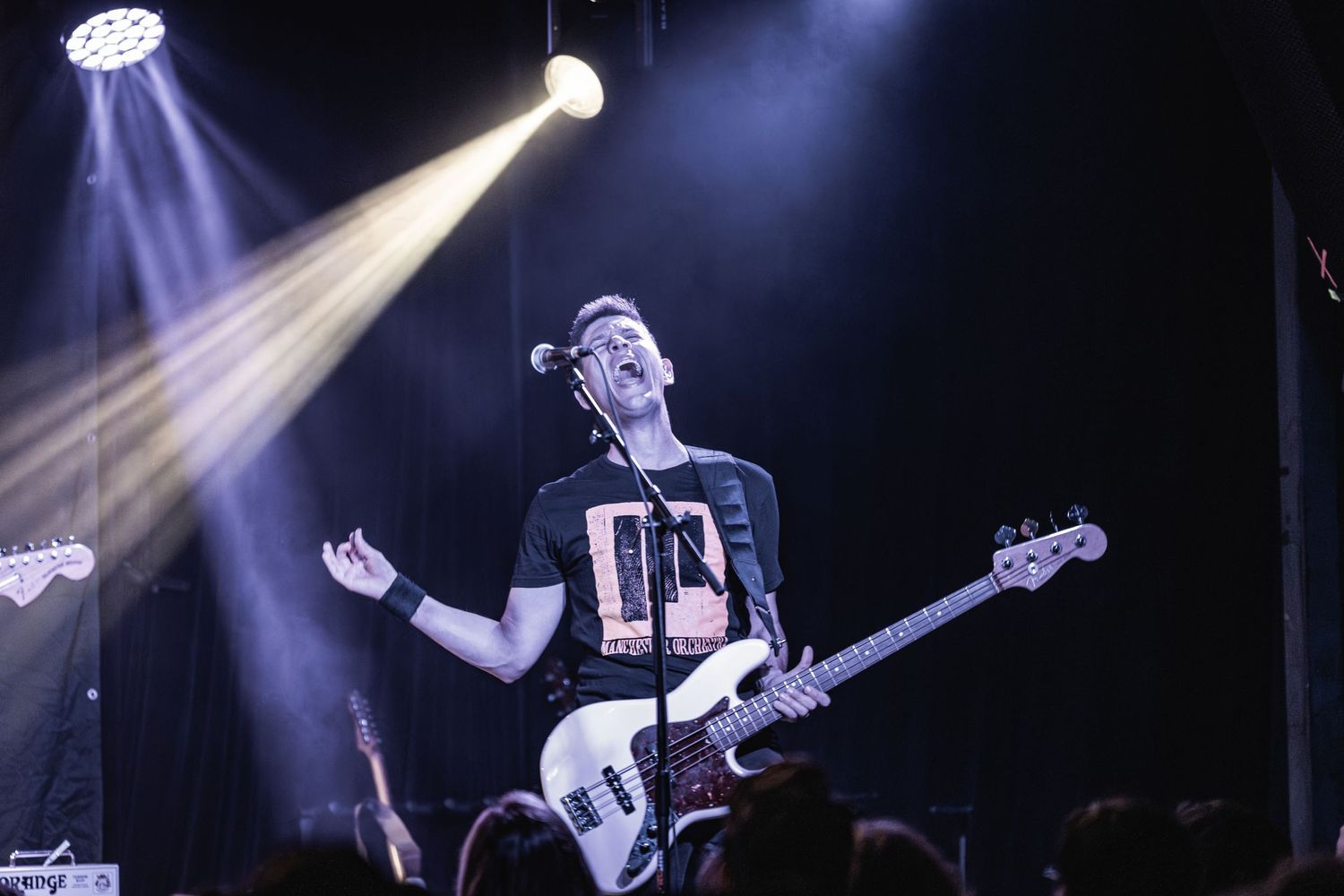 Bass guitarist performs passionately under dramatic blue and white spotlights at a concert.