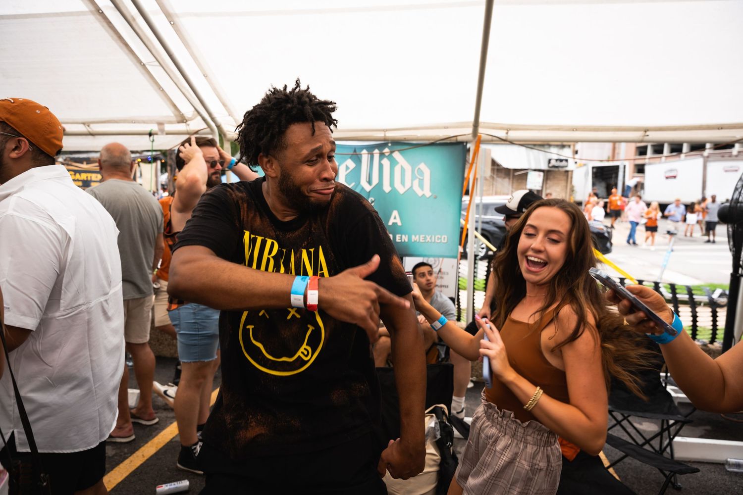 People dancing and celebrating at an outdoor festival under a white tent.