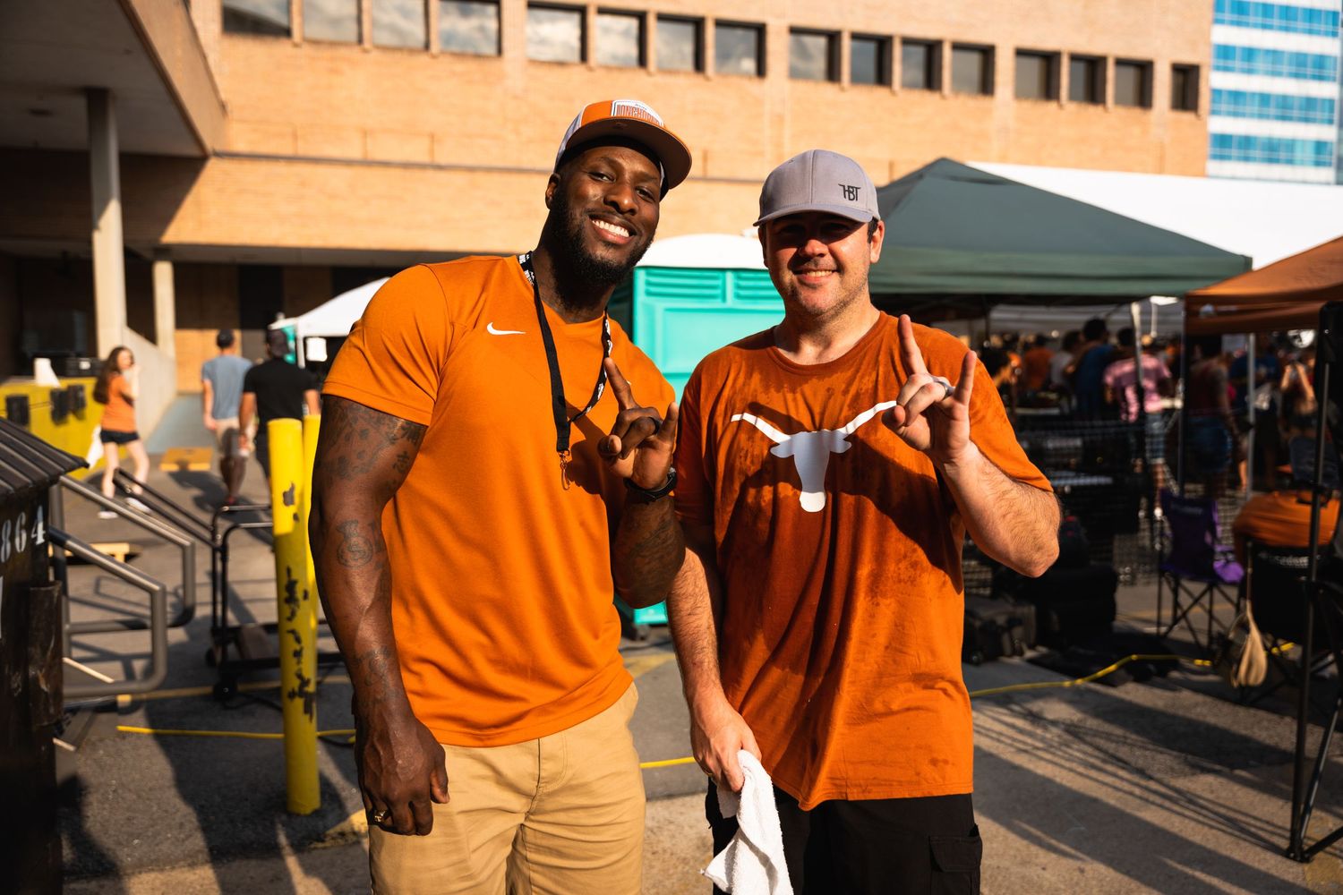 Two enthusiastic fans in orange and brown jerseys pose together at a sports event.