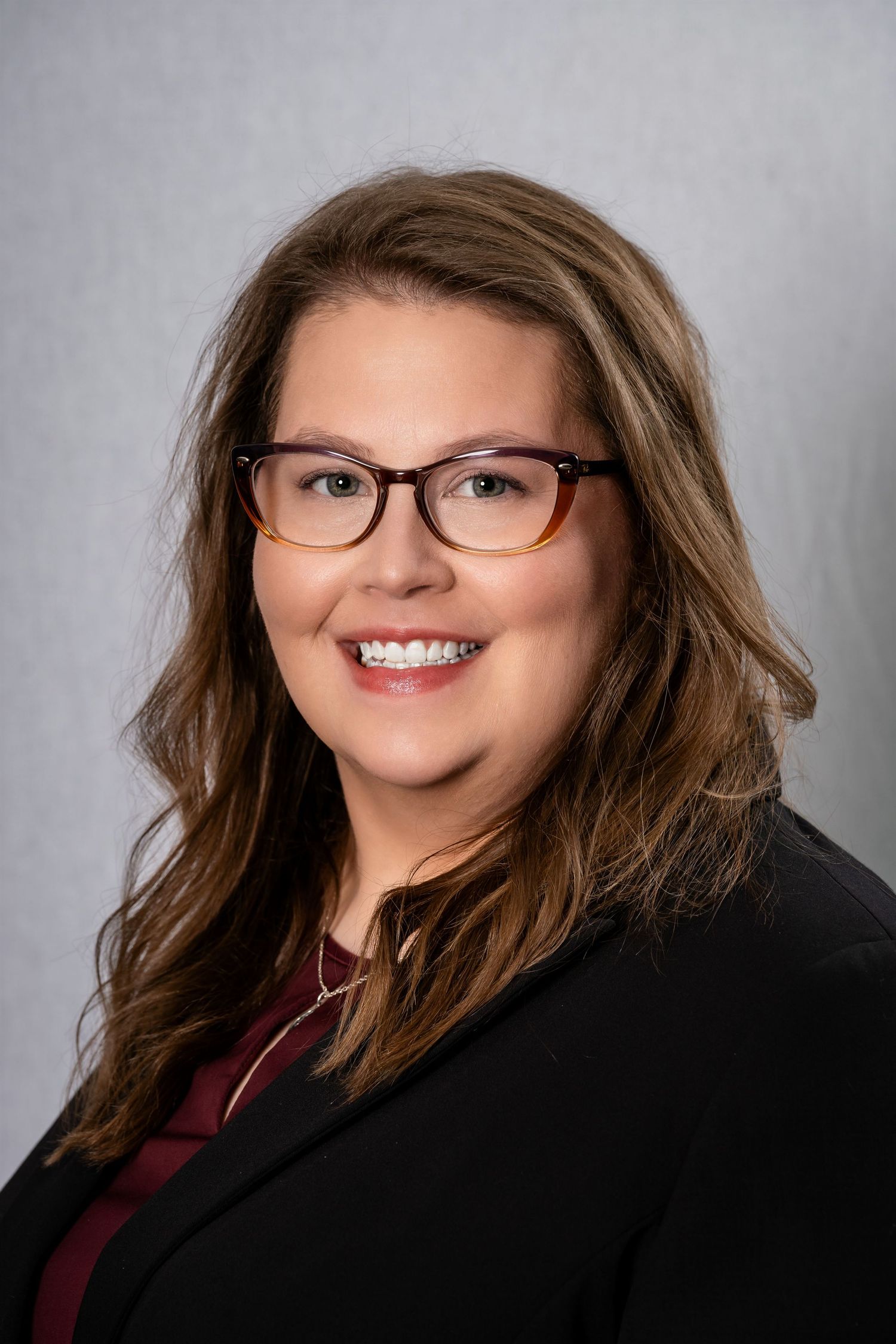 Professional headshot of person in glasses and blazer against neutral background.